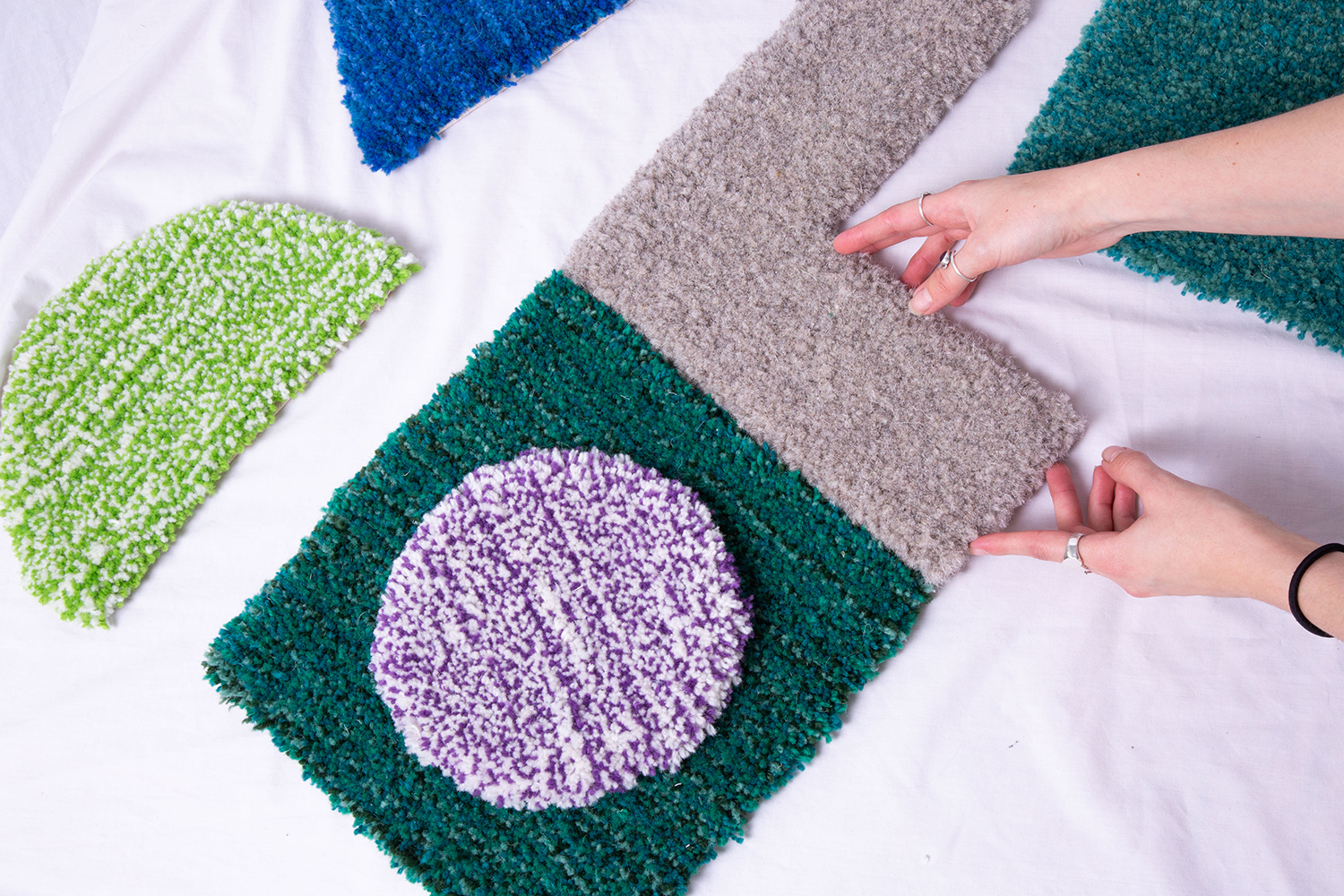 Blue, green, purple and grey geometric rug pieces being put together on a white background.