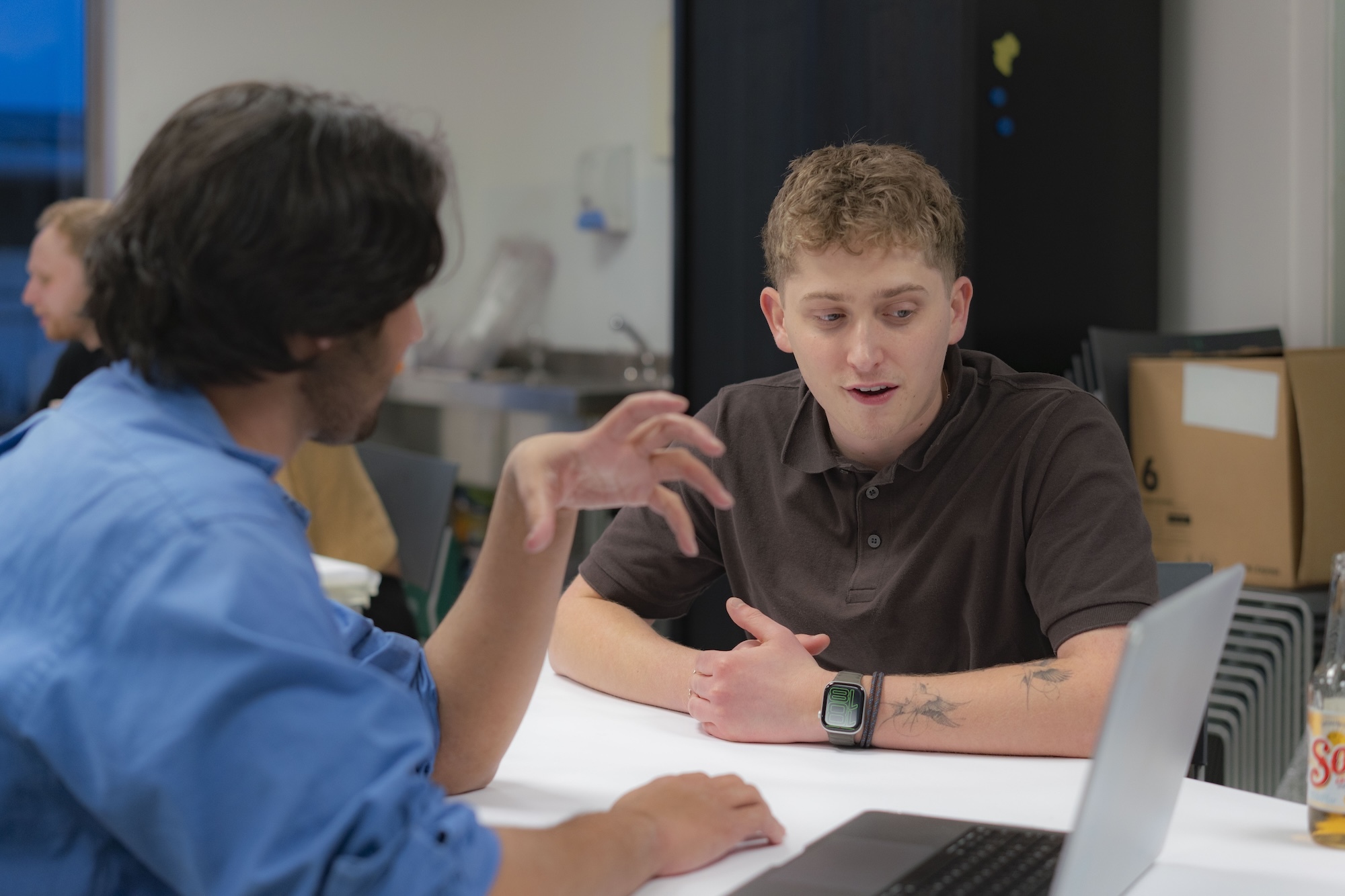 T Felton sits with a BA (Hons) Graphic Design student at a desk, with laptop and papers visible.