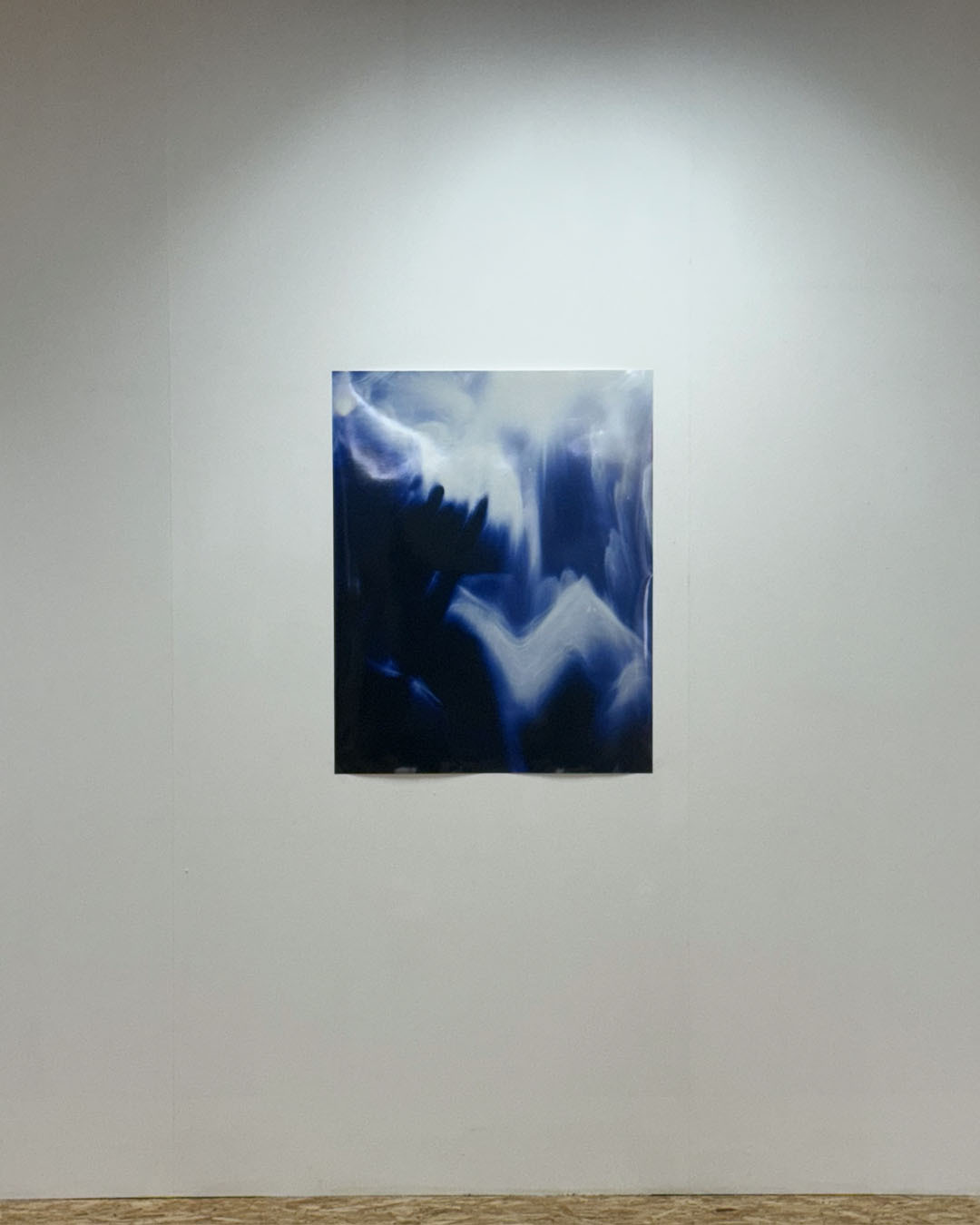 Small rectangular artwork with flowing blue and white abstract forms mounted on white gallery wall.