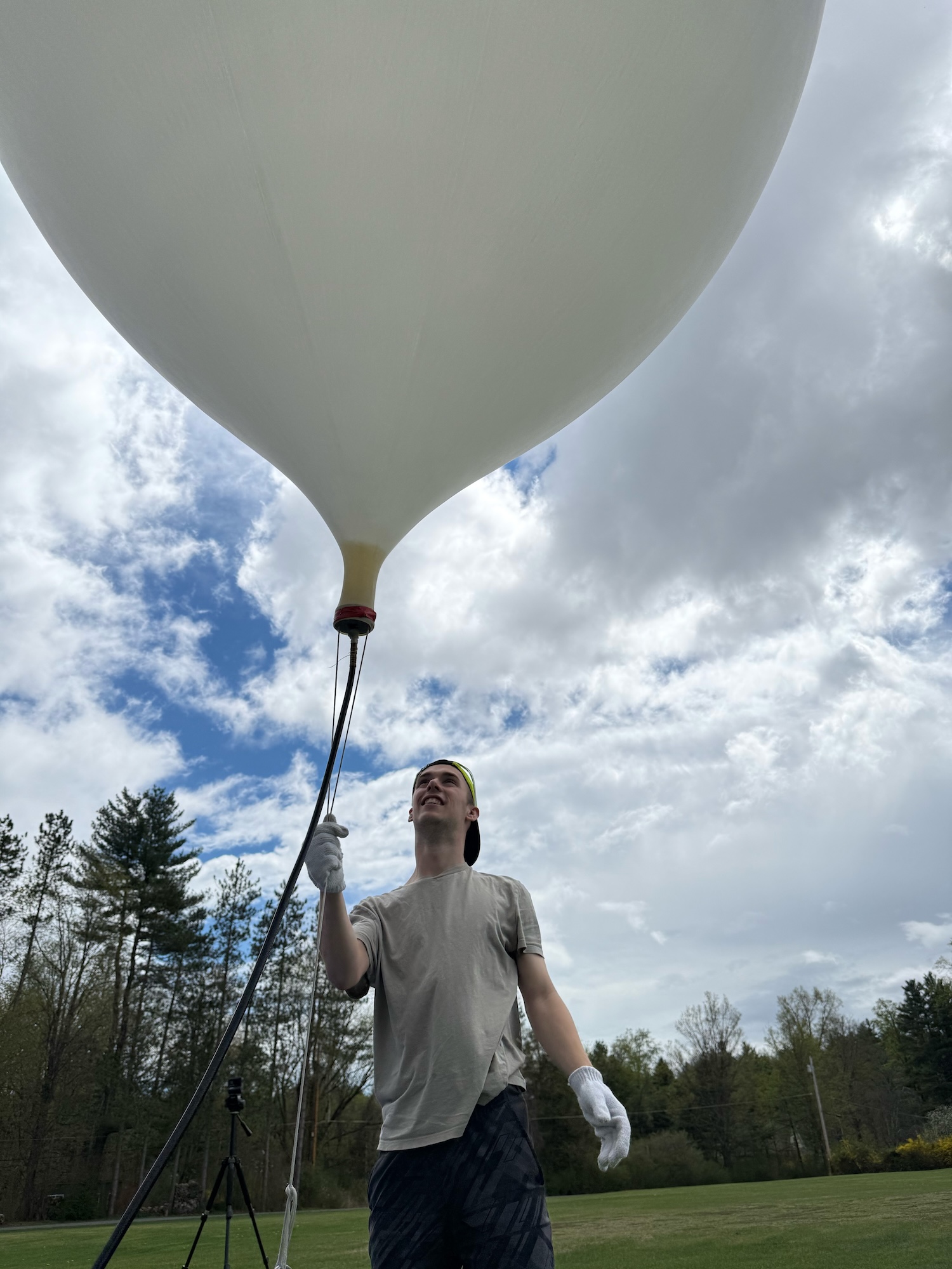 T Liggett standing in a field under a cloudy sky with a large weather balloon.