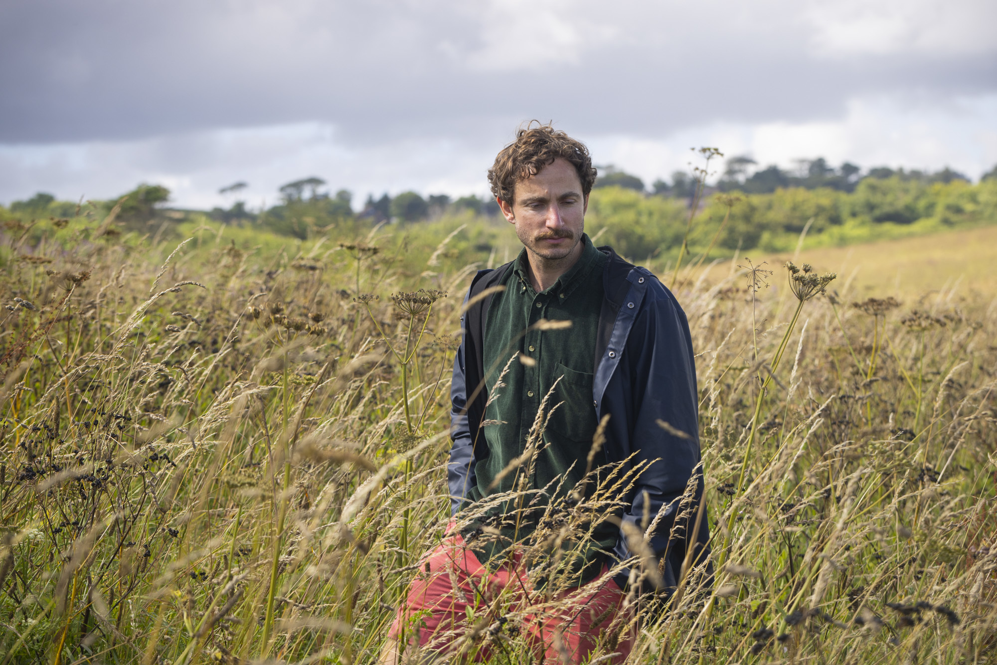 Tom Massey walking through a field with long grass and plants.
