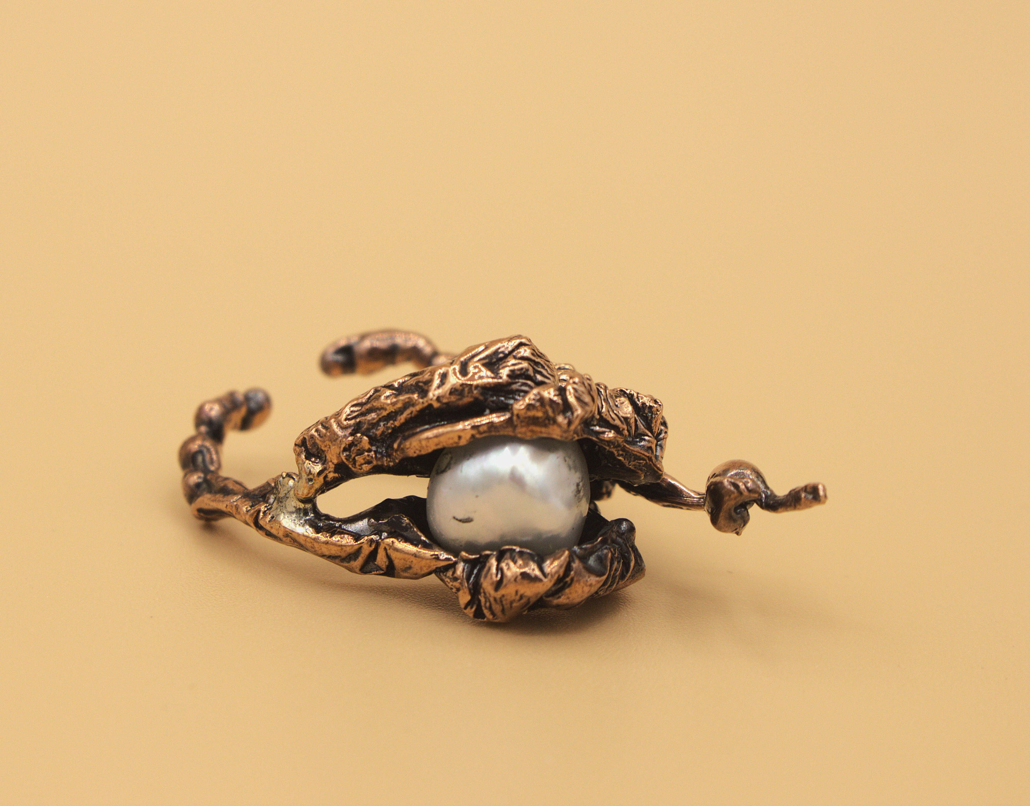 Piece of gold-coloured jewellery with a pearl-like stone in the centre, on a pale yellow background.
