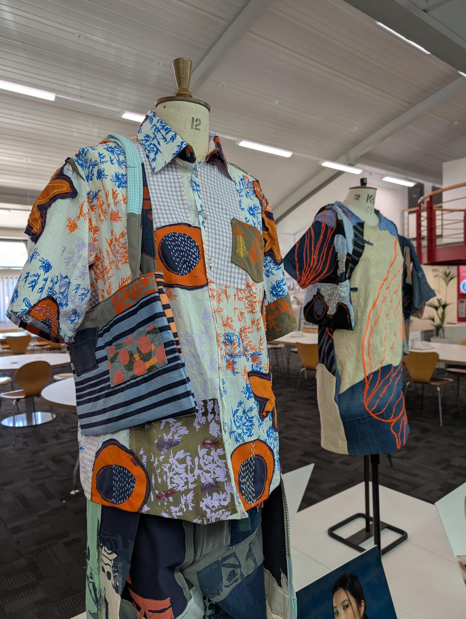 Two garments on mannequins in white room with fluorescent lighting. Patchwork designs featuring orange circles, blue florals, stripes, and geometric patterns in mixed fabrics.
