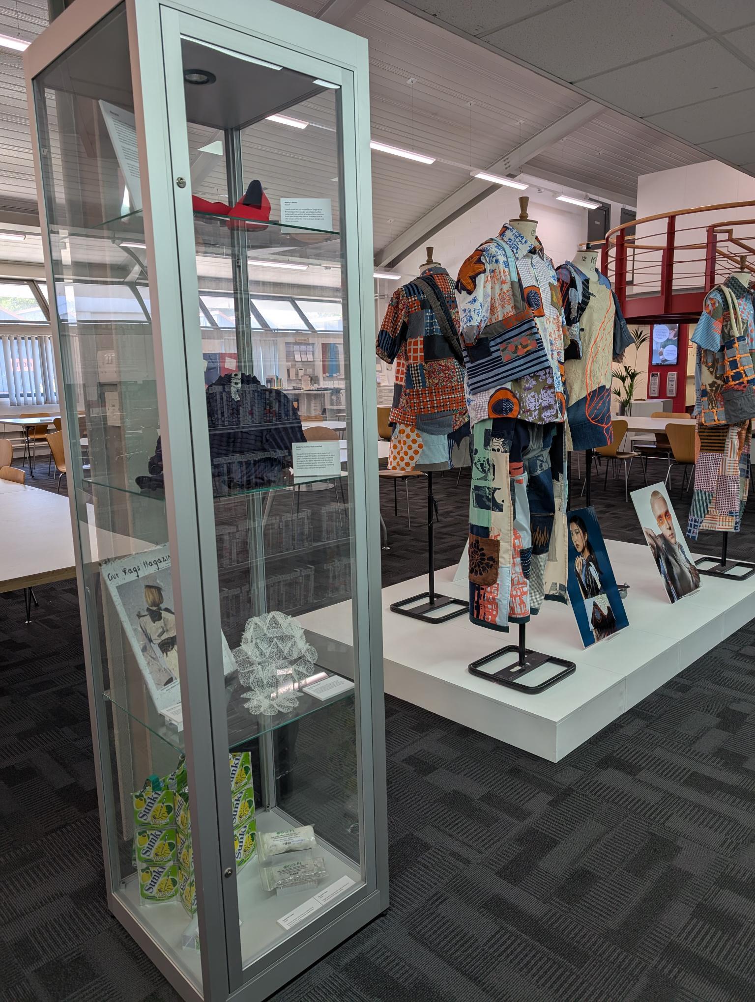 Museum display with glass cabinet containing textiles and platform showing colourful patchwork garments on mannequins.