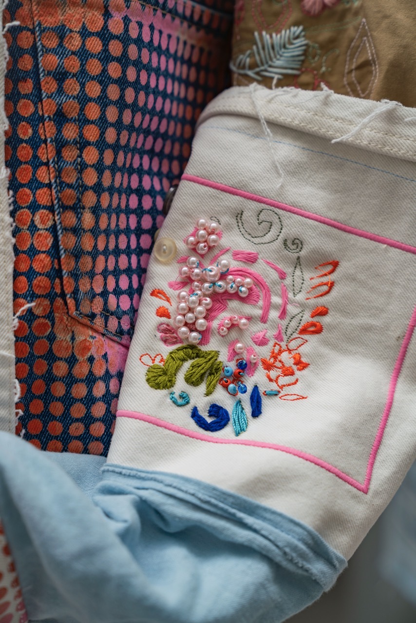 Close-up on Trash to Treasure clothing piece, showing detailed, intricate sewing work with pink beads and small, detailed pink floral work.