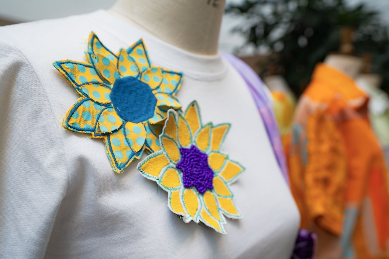 White top with decorative sunflower patches - one blue and yellow checkered with blue centre, one yellow with purple centre