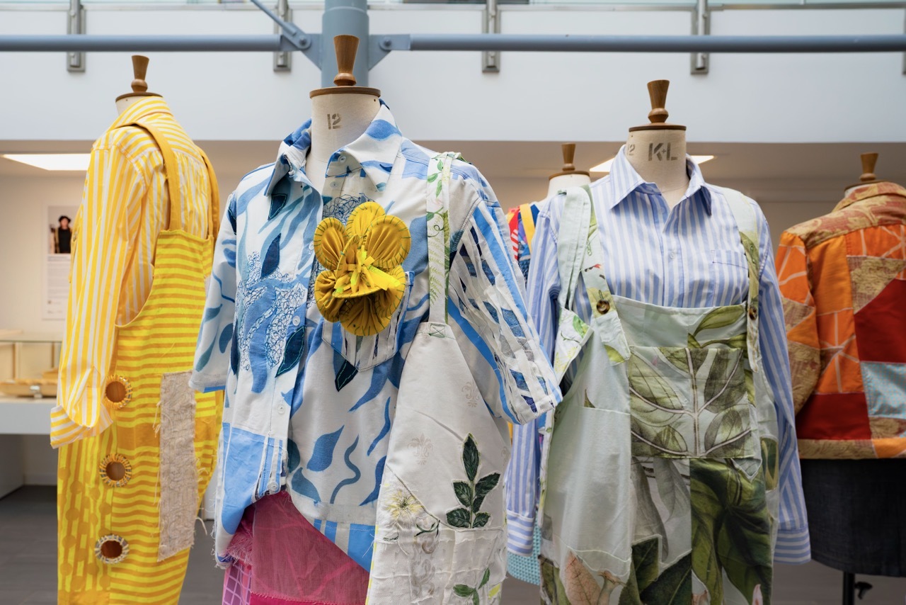 Three mannequins displaying colourful clothing: yellow knit cardigan, blue floral shirt, and green patterned dress in bright retail space