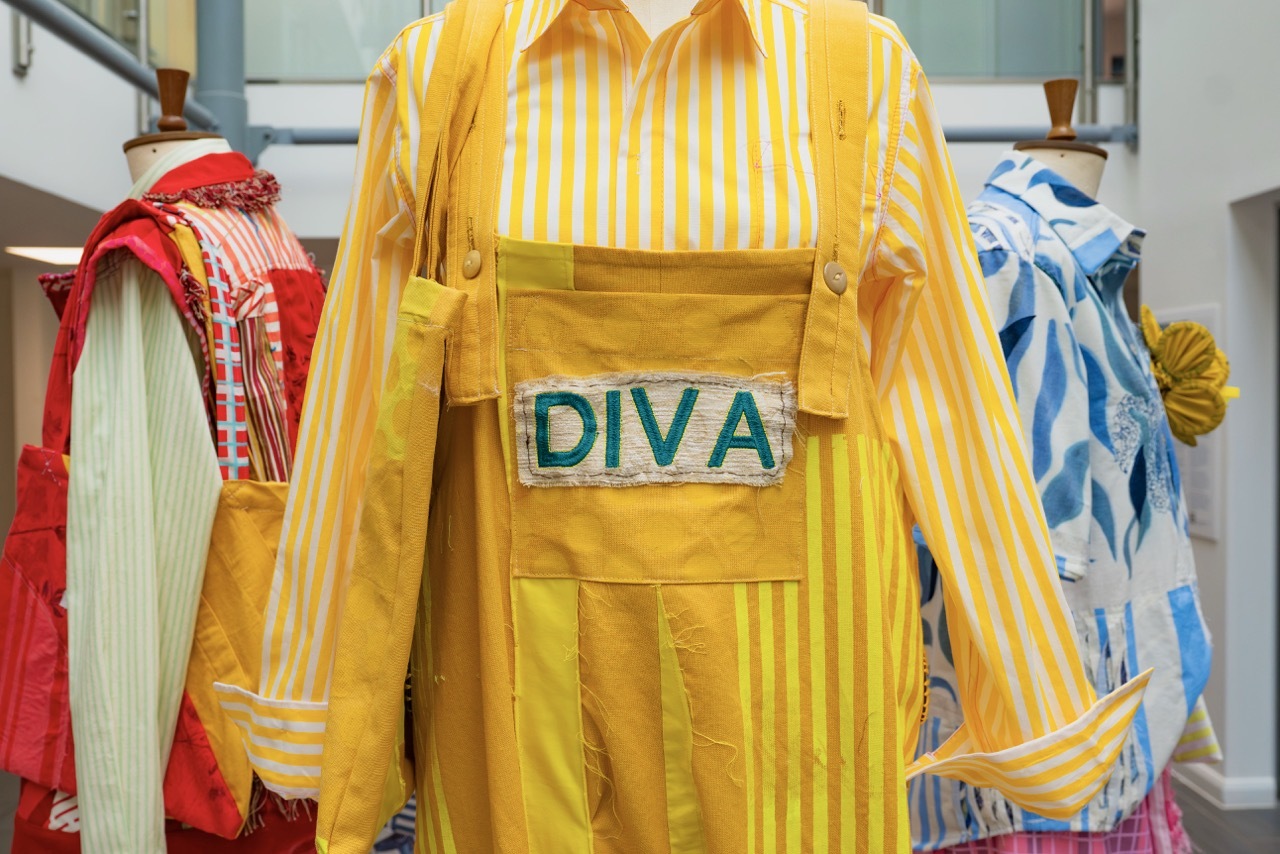 Yellow and white striped shirt with yellow apron displaying 'DIVA' text, flanked by red and blue patterned garments on display