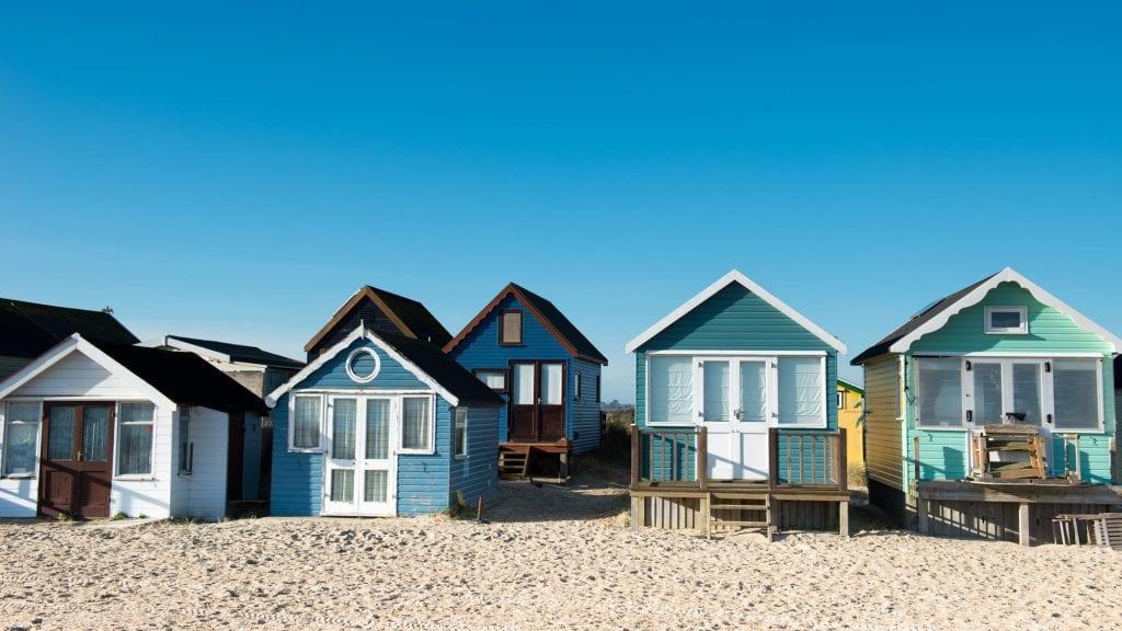 Two rows of colourful beach huts on the sand.