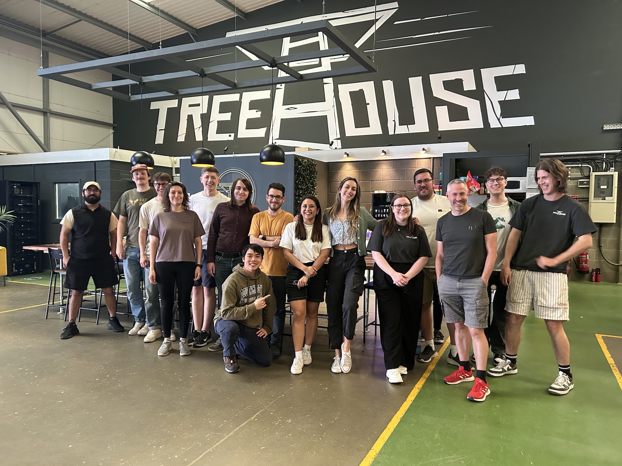 Group of people standing and sitting in warehouse space beneath large white "TREEHOUSE" sign on dark wall.