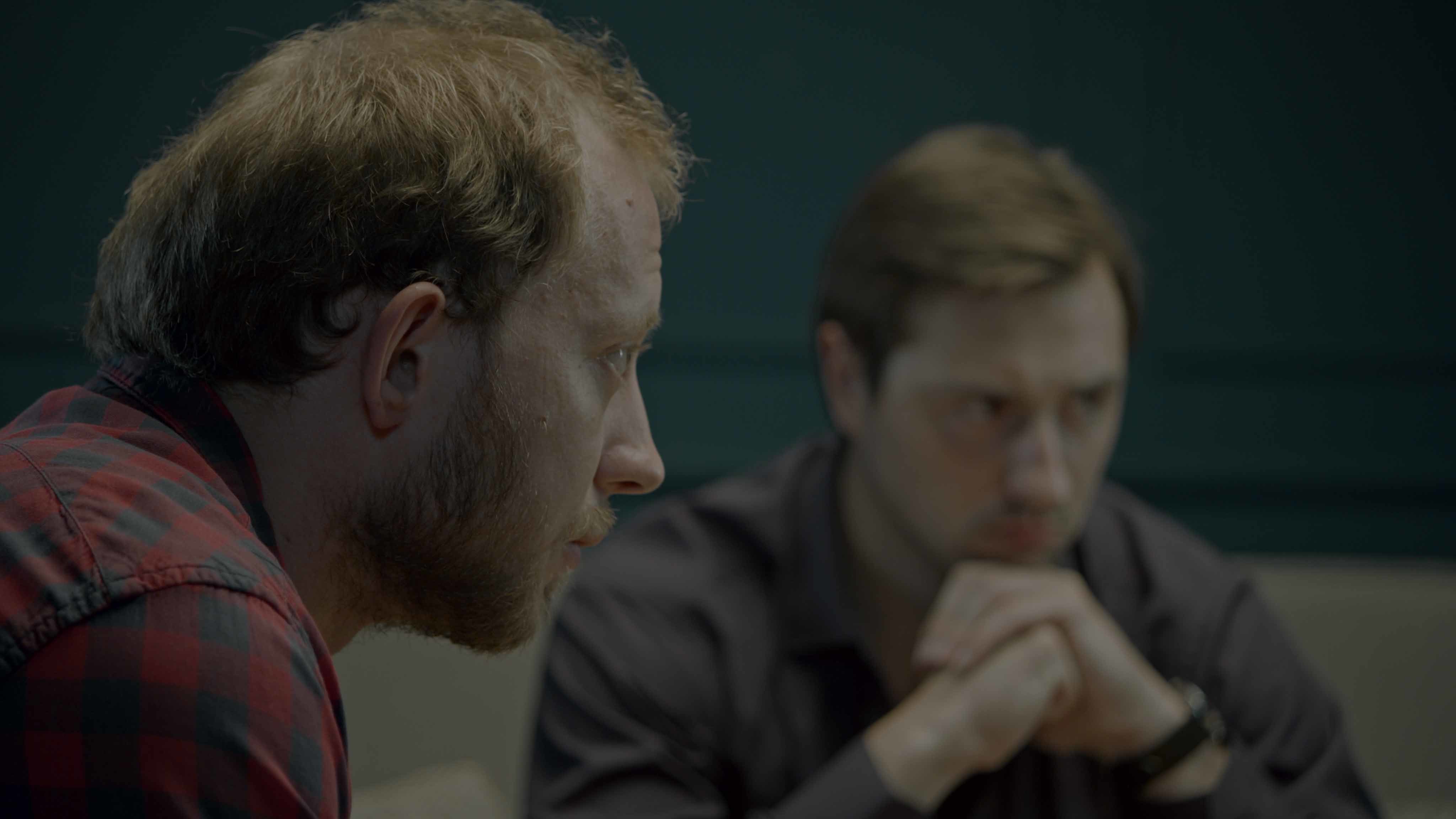 Two young men look pensively off-camera