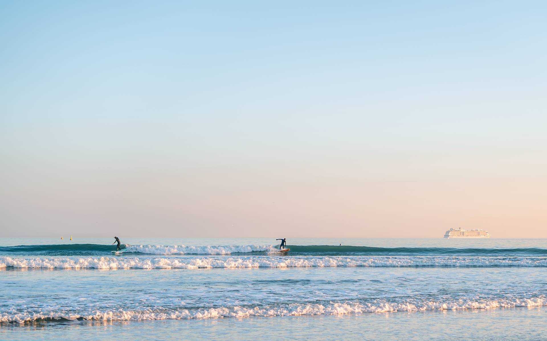 Two surfers riding waves in the sea, while two other waves come towards the shore.
