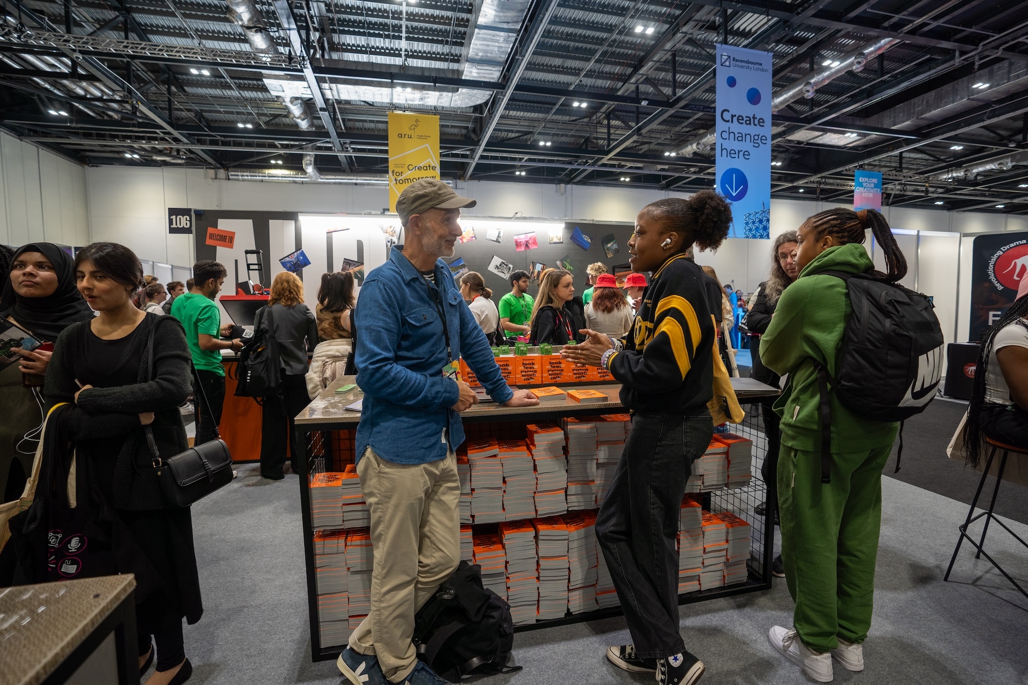 An academic talks to attendees at the Arts University Bournemouth stand at a UCAS event.