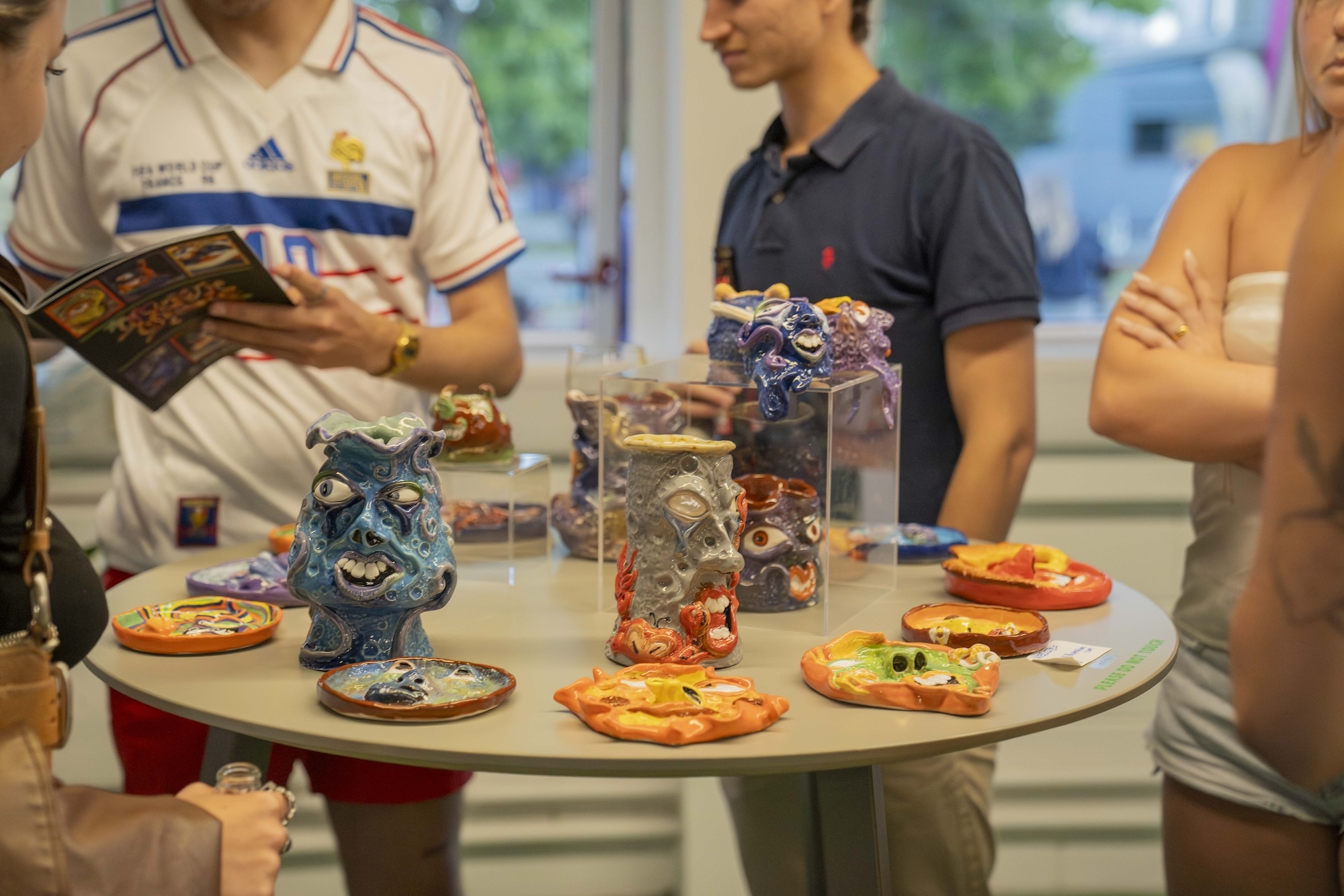 A selection of colourful ceramic sculptures with different facial designs on them, all displayed on a round table at AUB's 2024 Summer Shows.