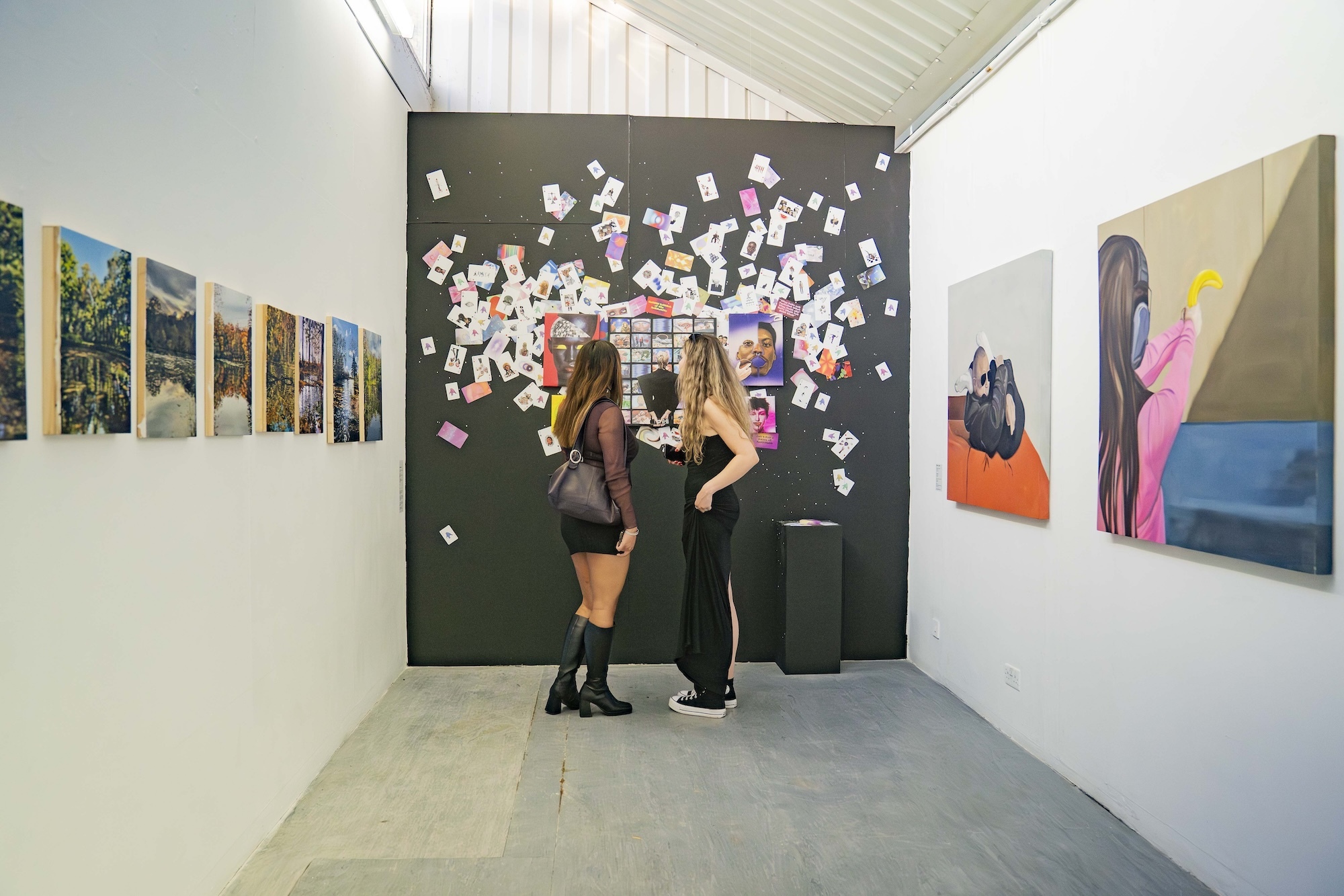 Two people looking at a colourful abstract mixed-media artwork on a black background, with paintings on the walls either side of them.