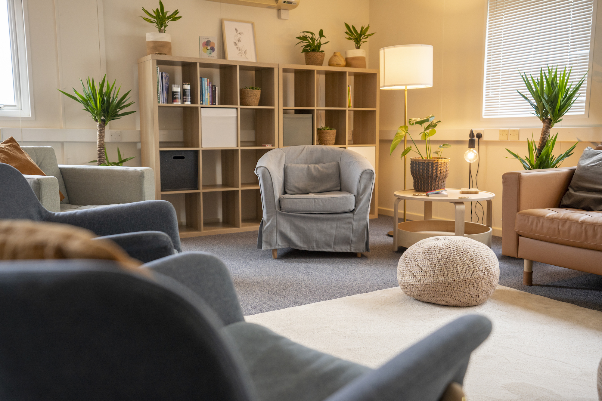 Armchairs and a sofa set around a white rug. A pair of square shelves are set up in the background.