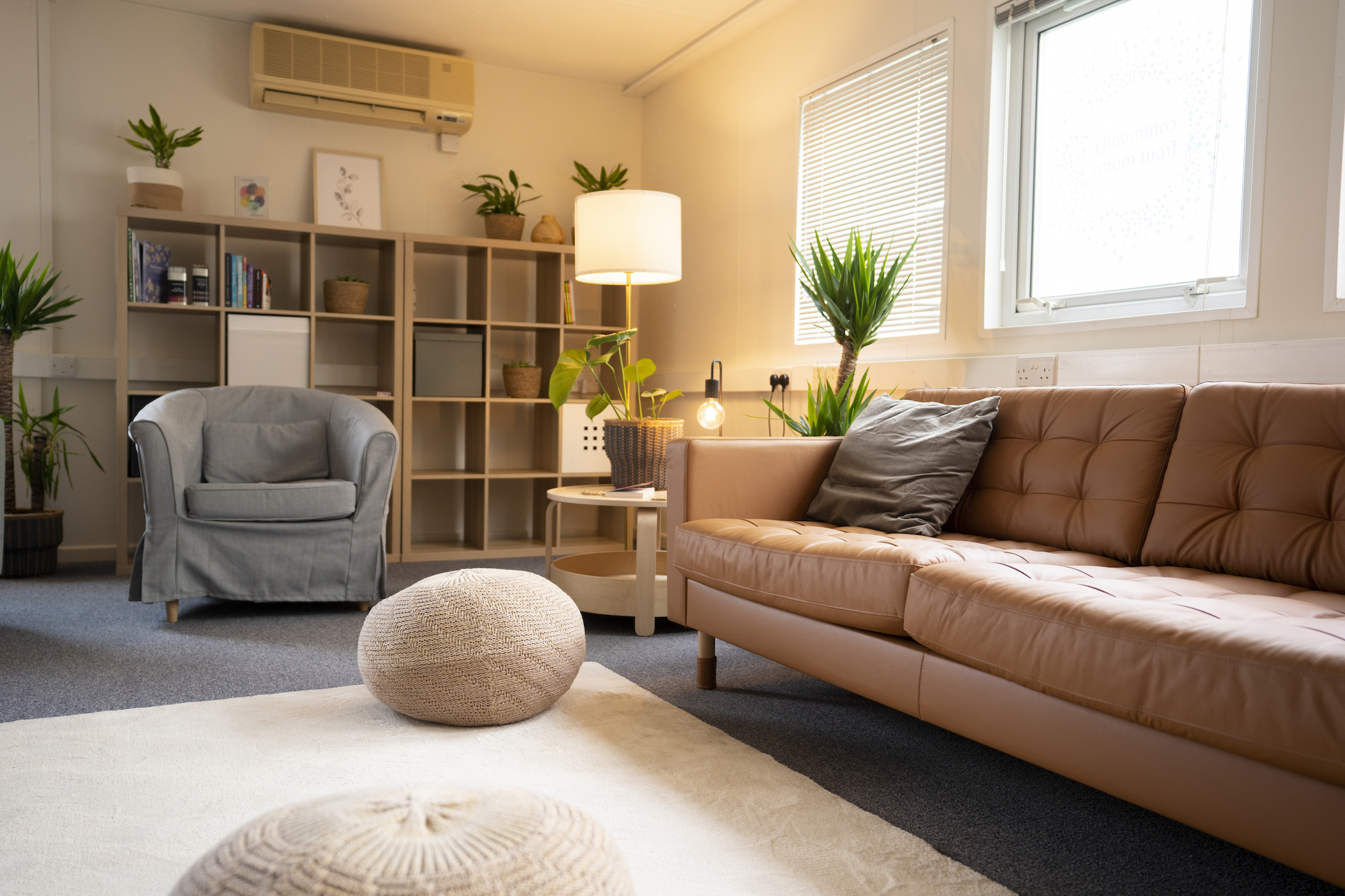 An armchair and a long sofa with a coffee table in between are set up around a white rug. A pair of beanbag footstools rest on the rug.