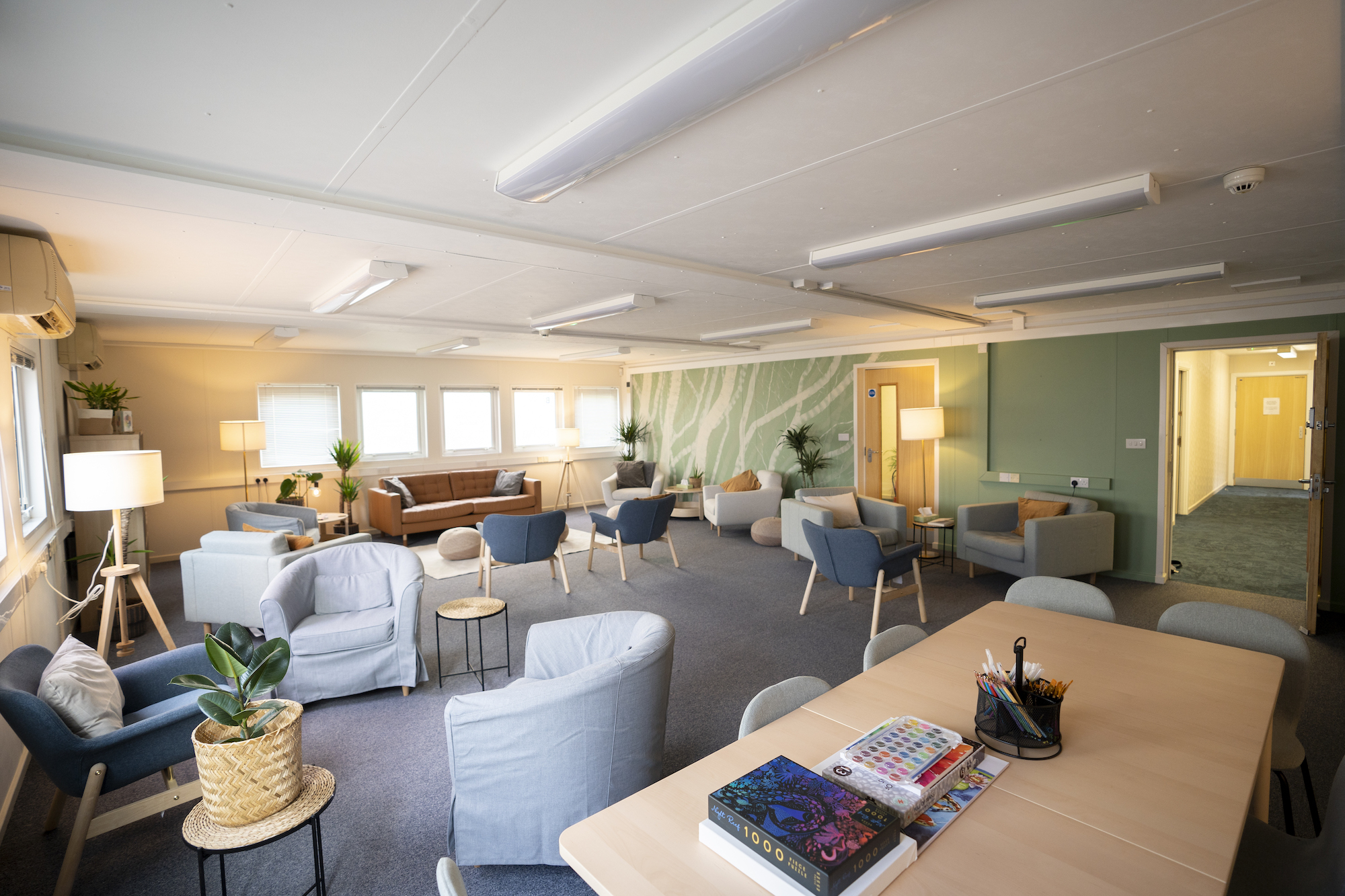Lounge-style room with a long table in the foreground, armchairs and sofas set up at regular intervals throughout the space.