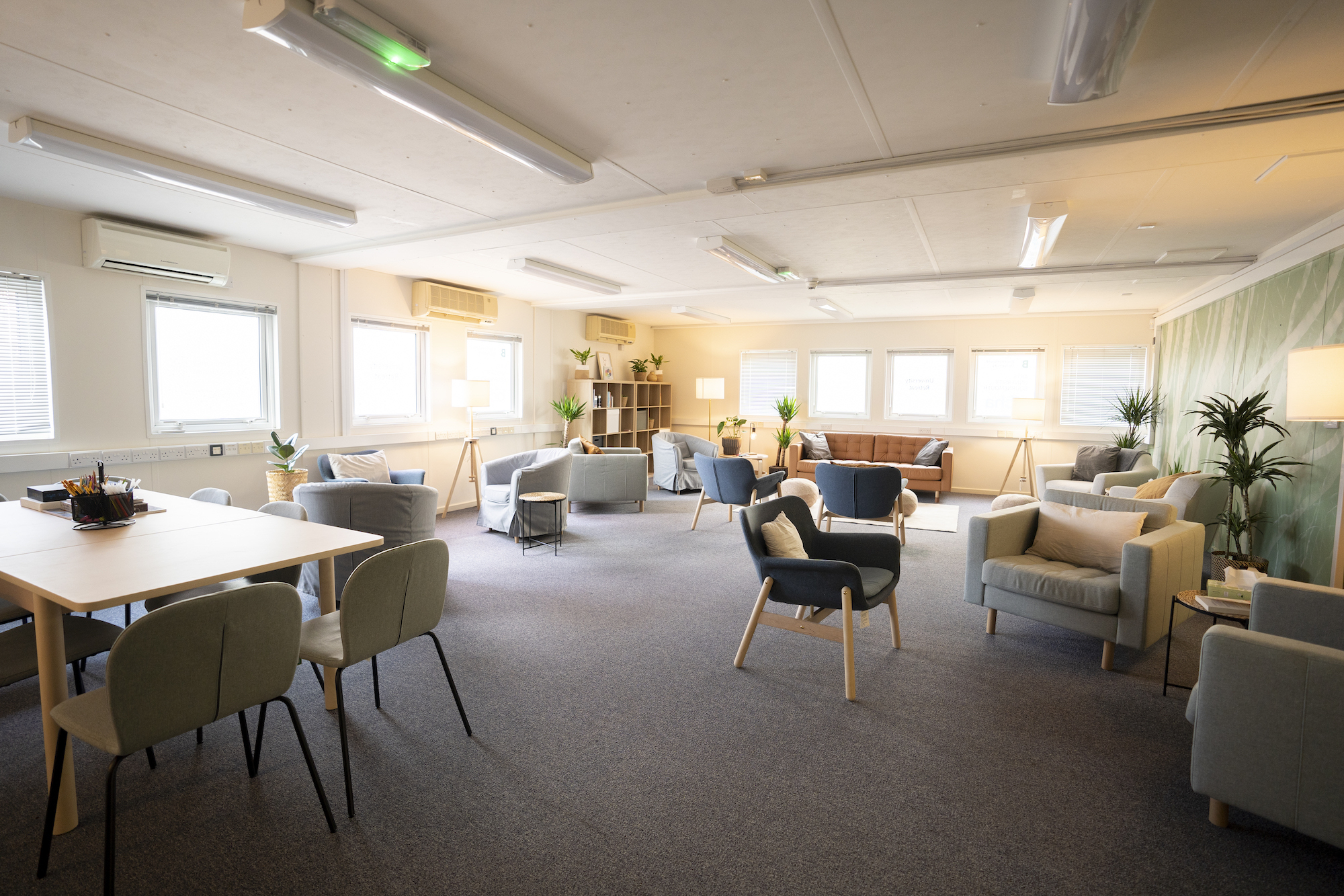 A wide shot of a community front room with tables, sofas and armchairs set up all around.