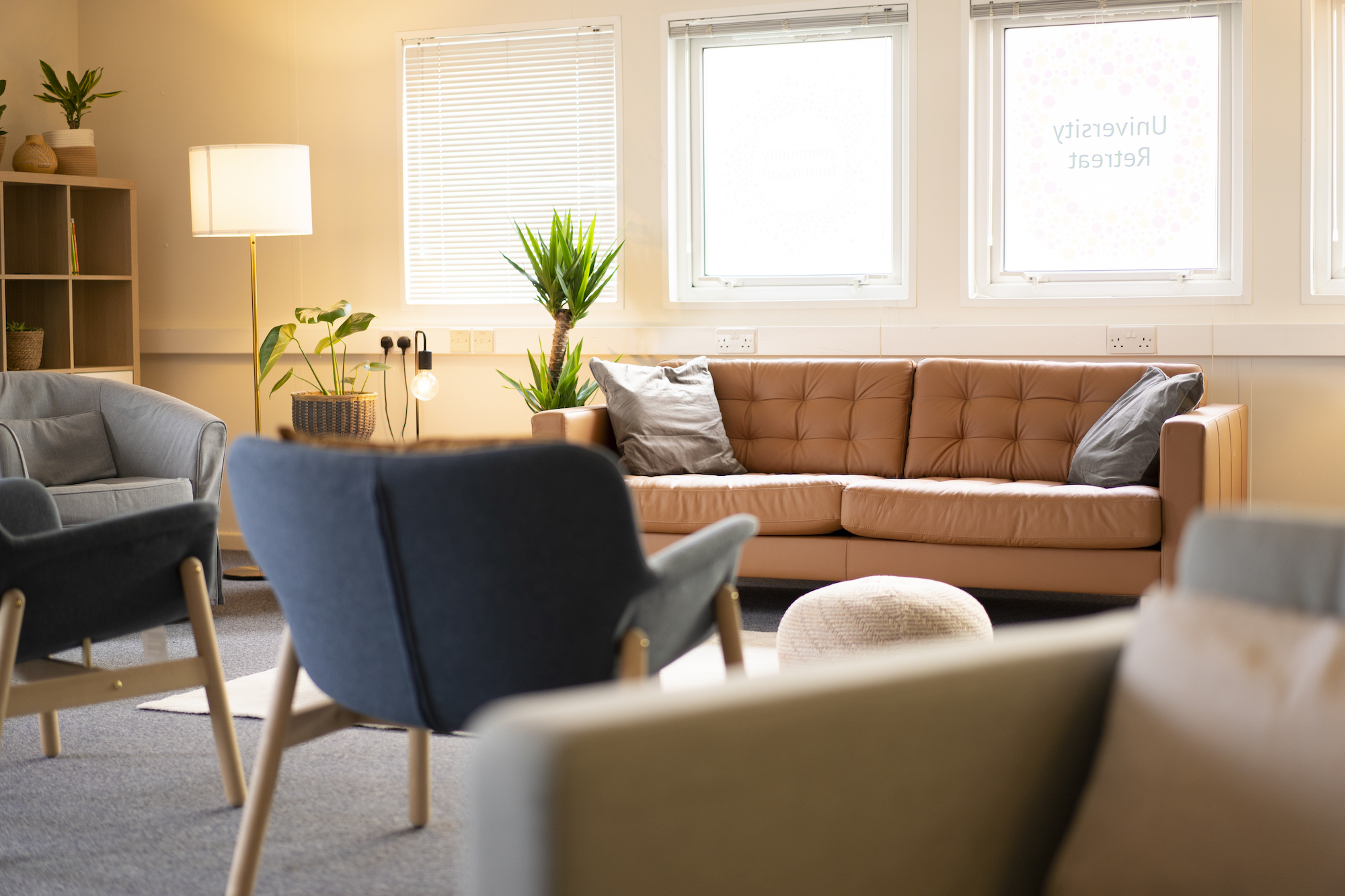 A long leather sofa sits under a pair of windows. Armchairs are arranged in a circle on the other side.