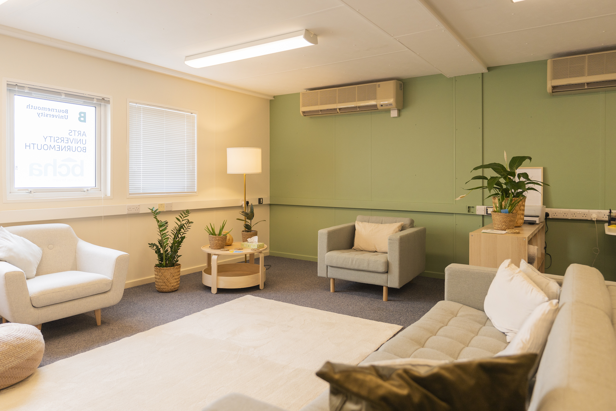 Two arm chairs with a plant and a coffee table in the corner. A long sofa sits at the other side.