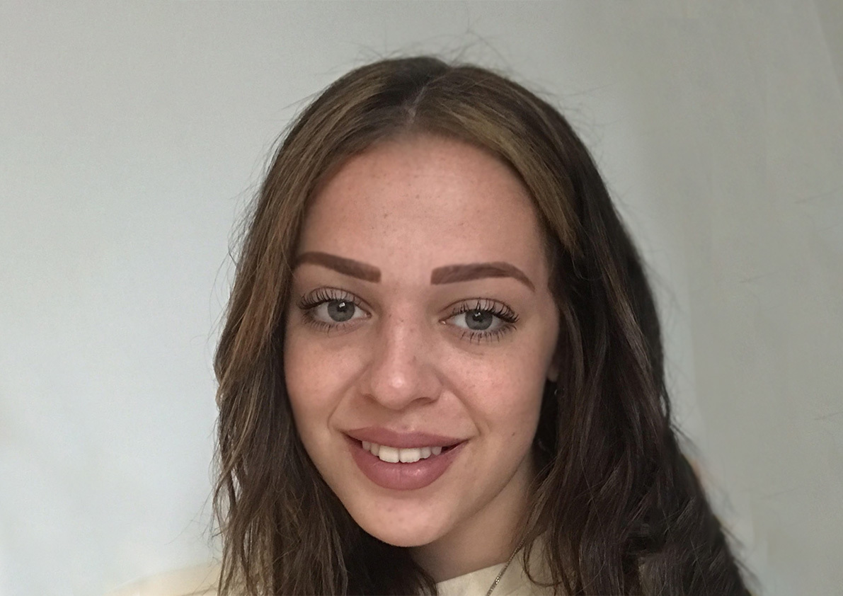 Young woman with long brown hair and green eyes smiling at camera against white background.