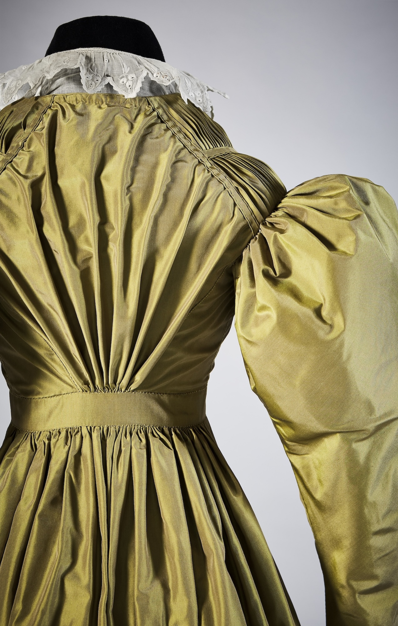 Close-up of the back and sleeve of a green 19th century-style silk dress.