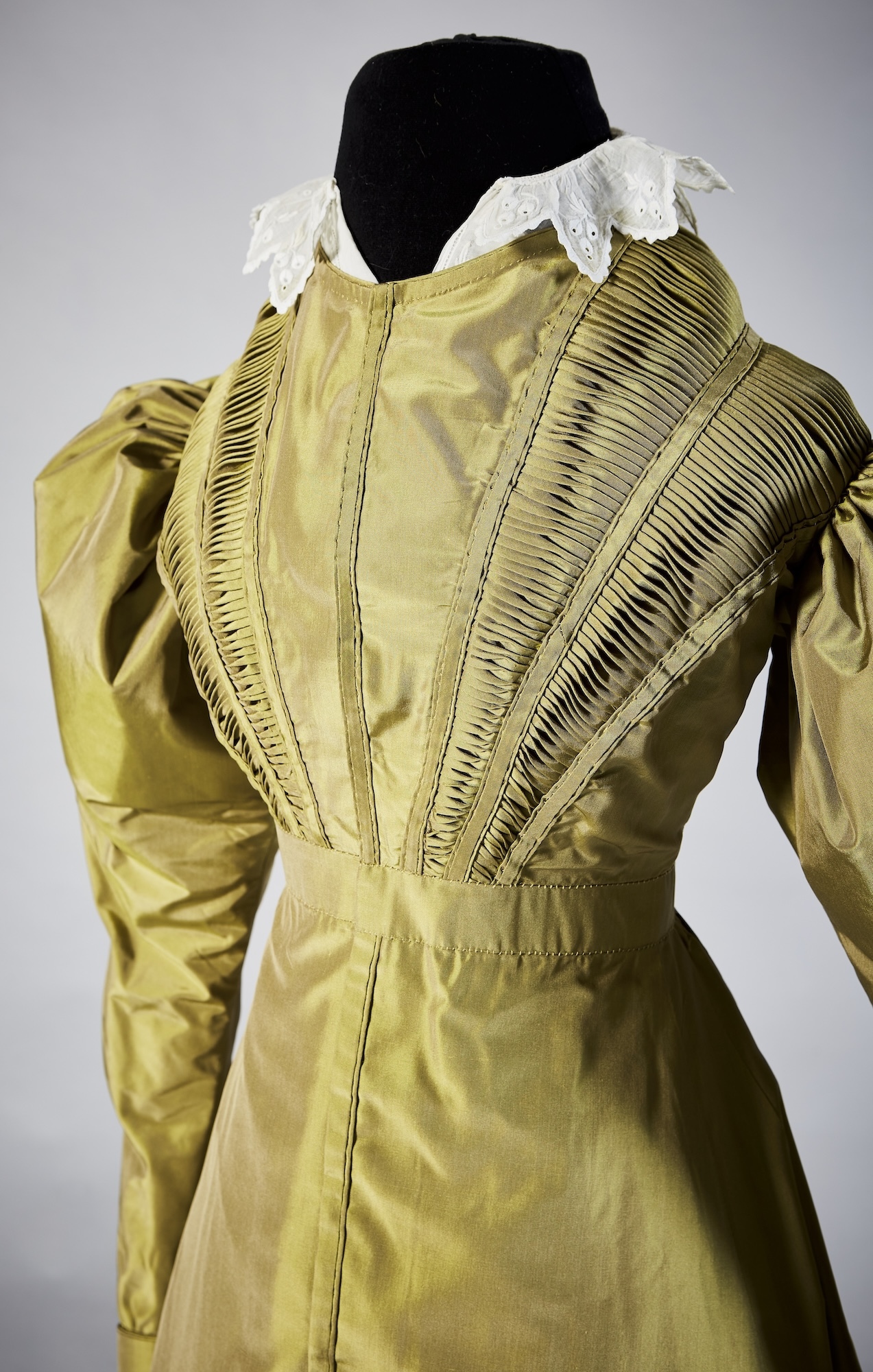 A 19th century-style, green silk dress with a white collar, viewed from the front, displayed on a mannequin.