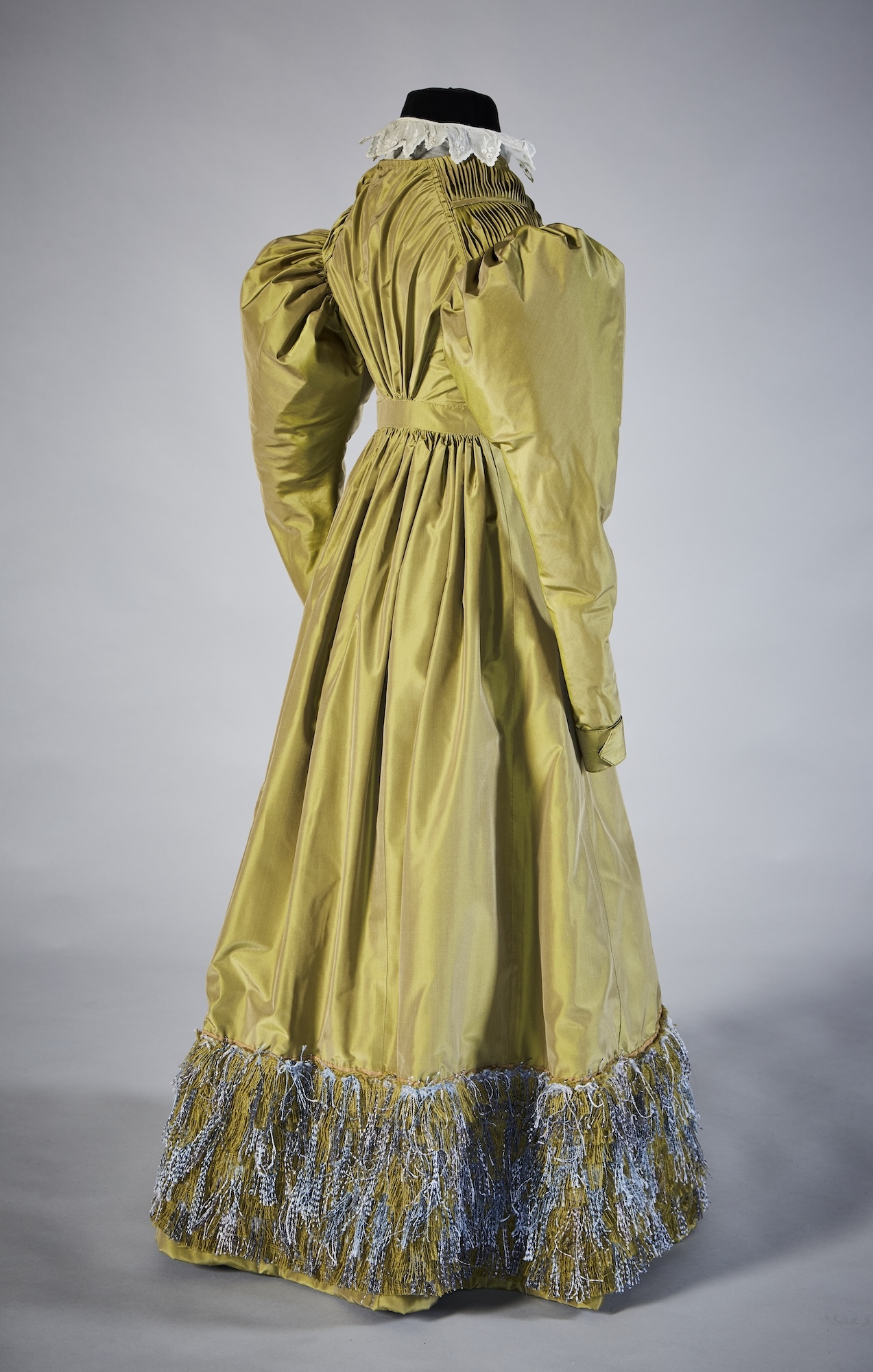 A green silk 19th century dress viewed from the back, displayed on a mannequin.