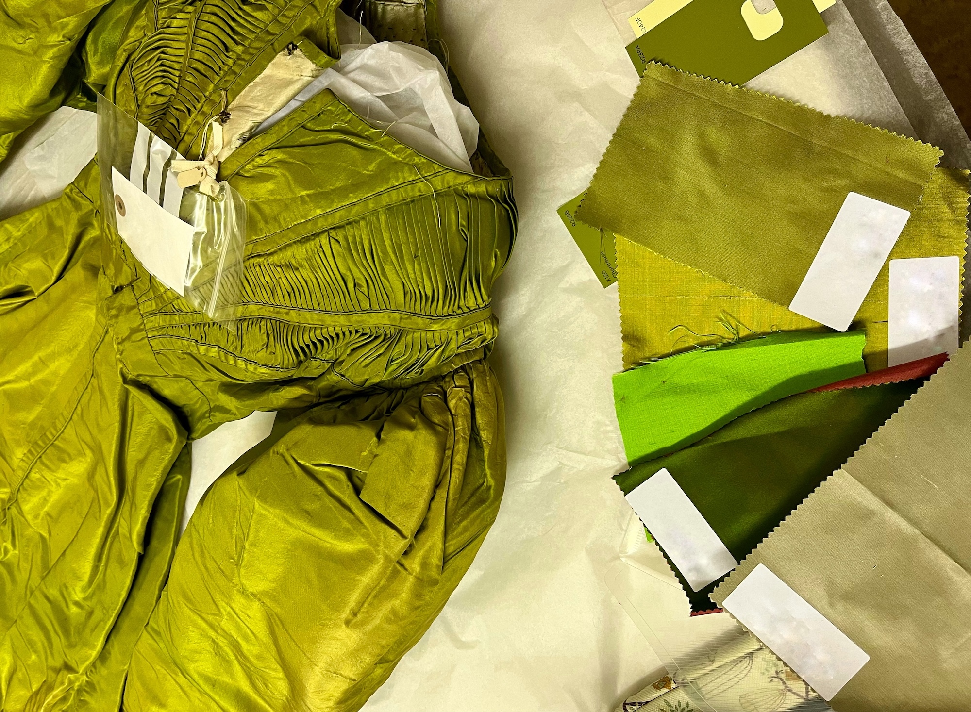 A green silk 19th century dress laid out next to several fabric samples in different shades of green.