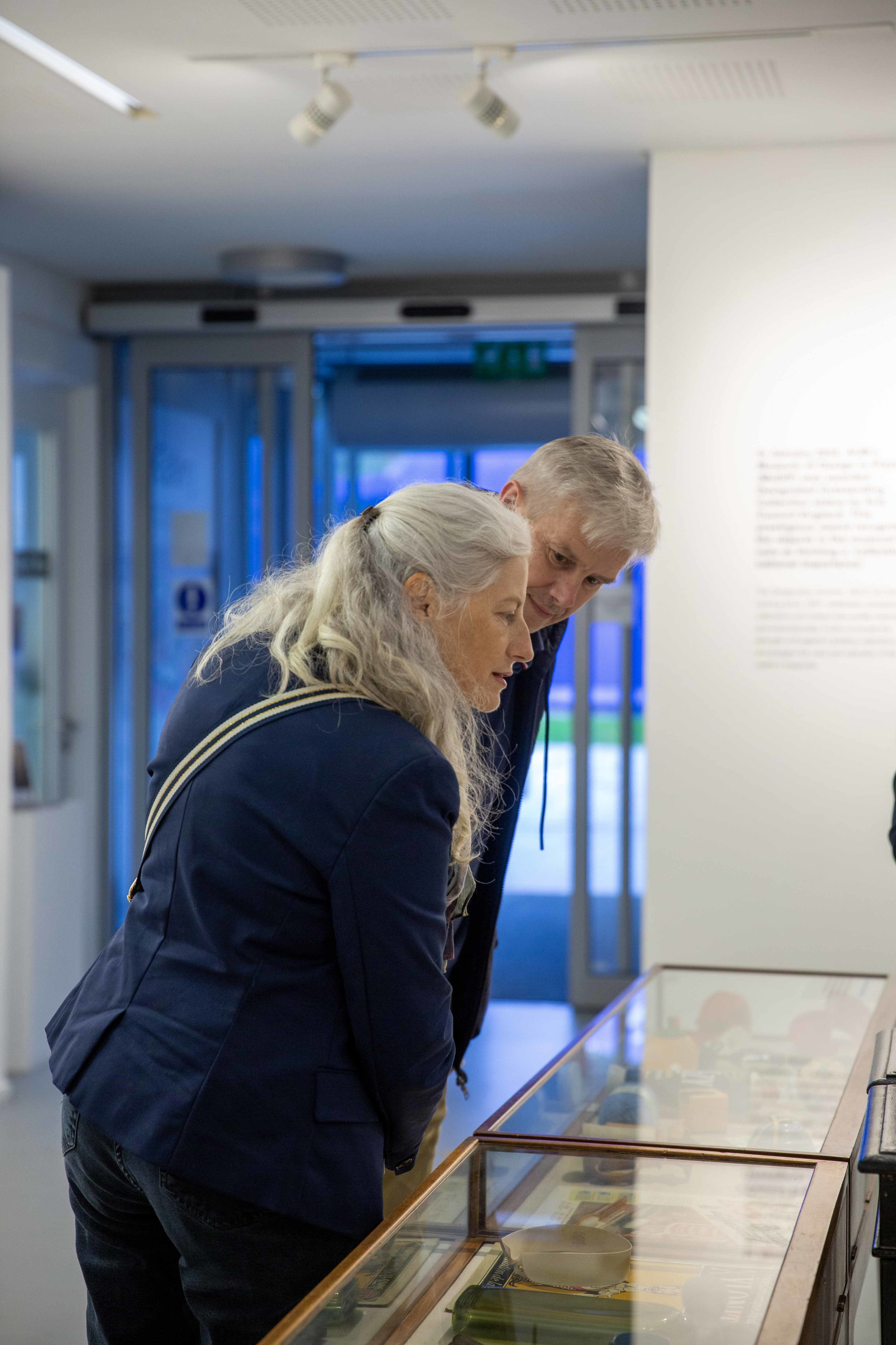 Two people looking over two glass display cases at a gallery exhibition.
