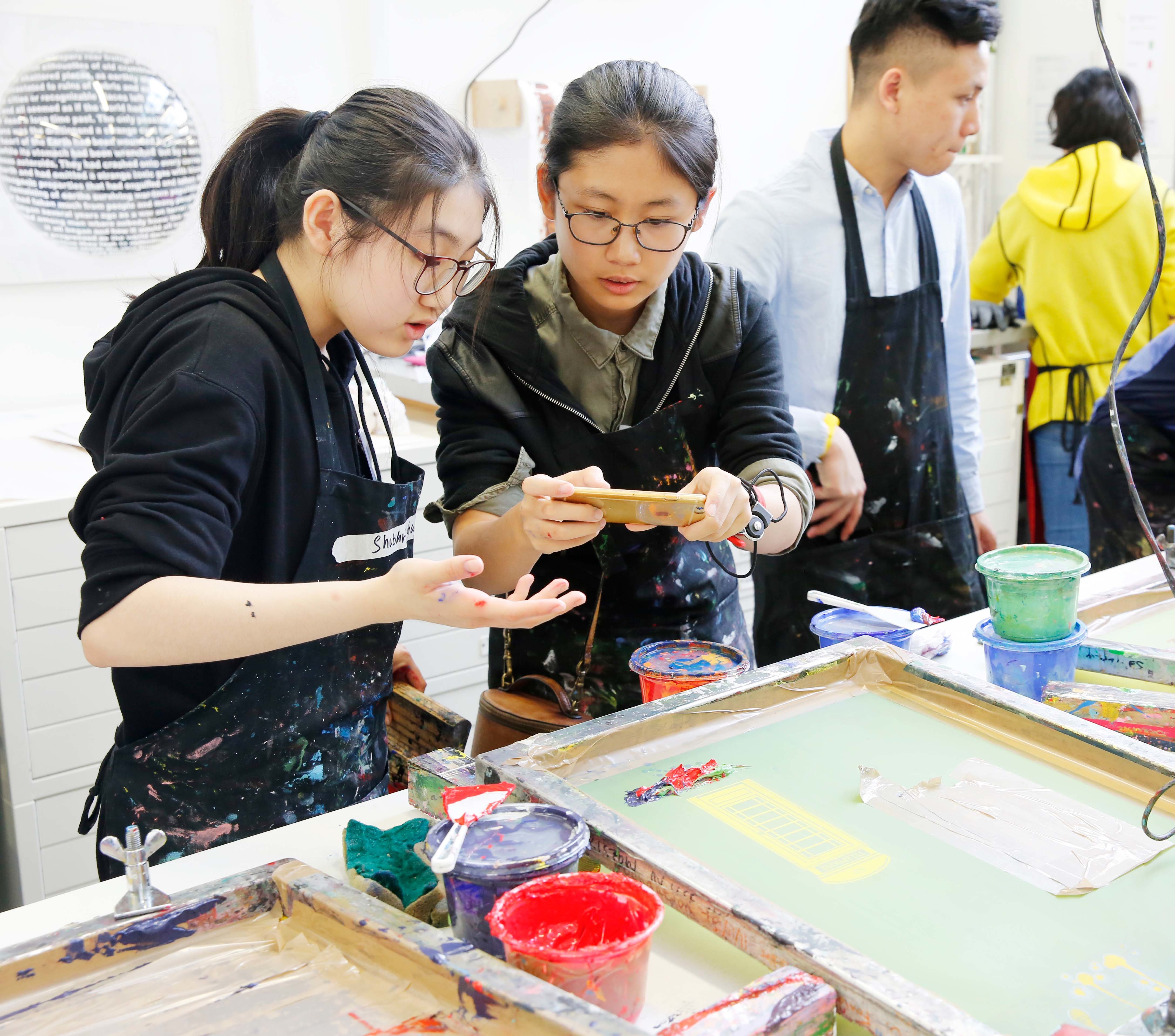 Students in the AUB print room holding tools with paint and screens around them.