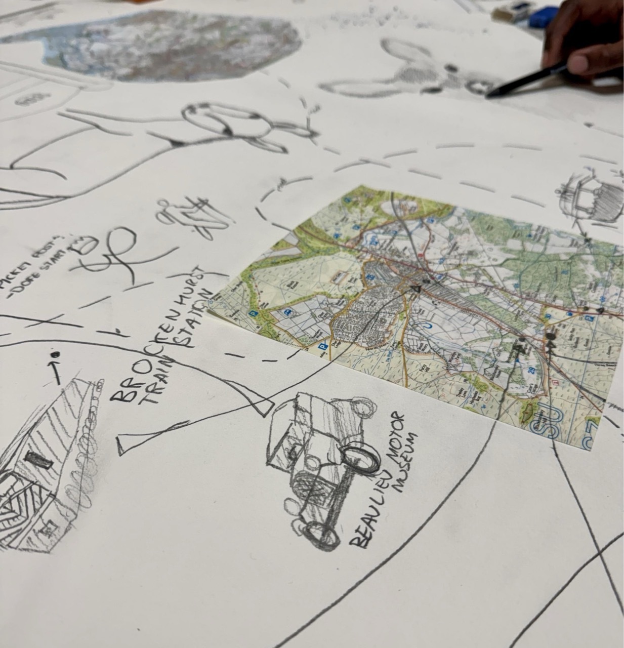 Scattered white papers with pencil sketches and handwritten notes, one sheet shows green and brown coloured map or diagram