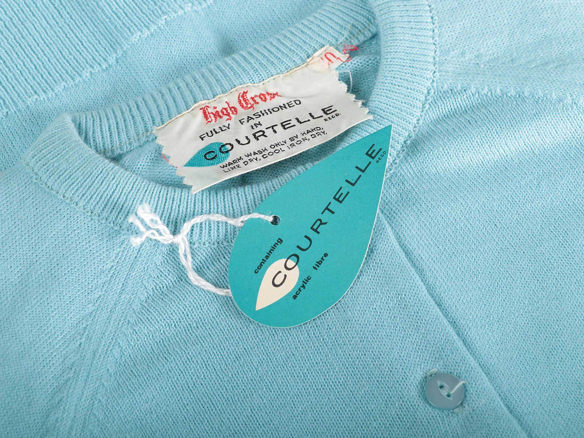 A close-up of a synthetic cardigan with a clothing tag with the brand name "Courtelle" on it.
