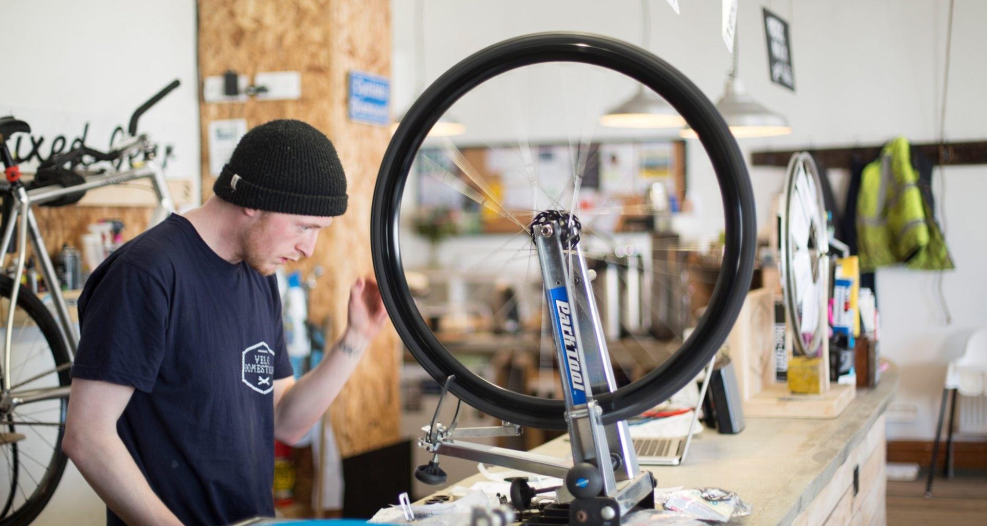 Man wearing a black knitted hat is inspecting a bicycle wheel in a workshop.