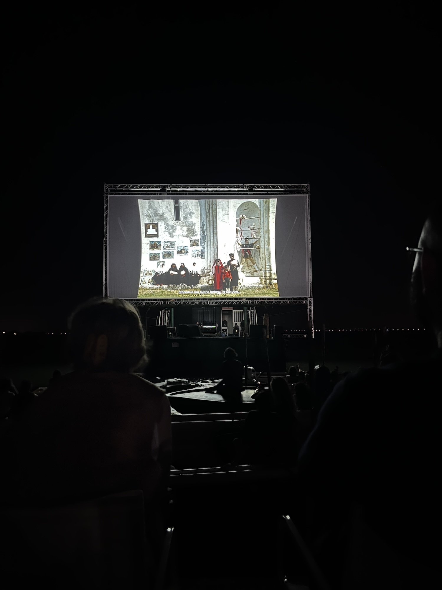 A large cinema screen with a film playing, viewed at night with darkness surrounding.