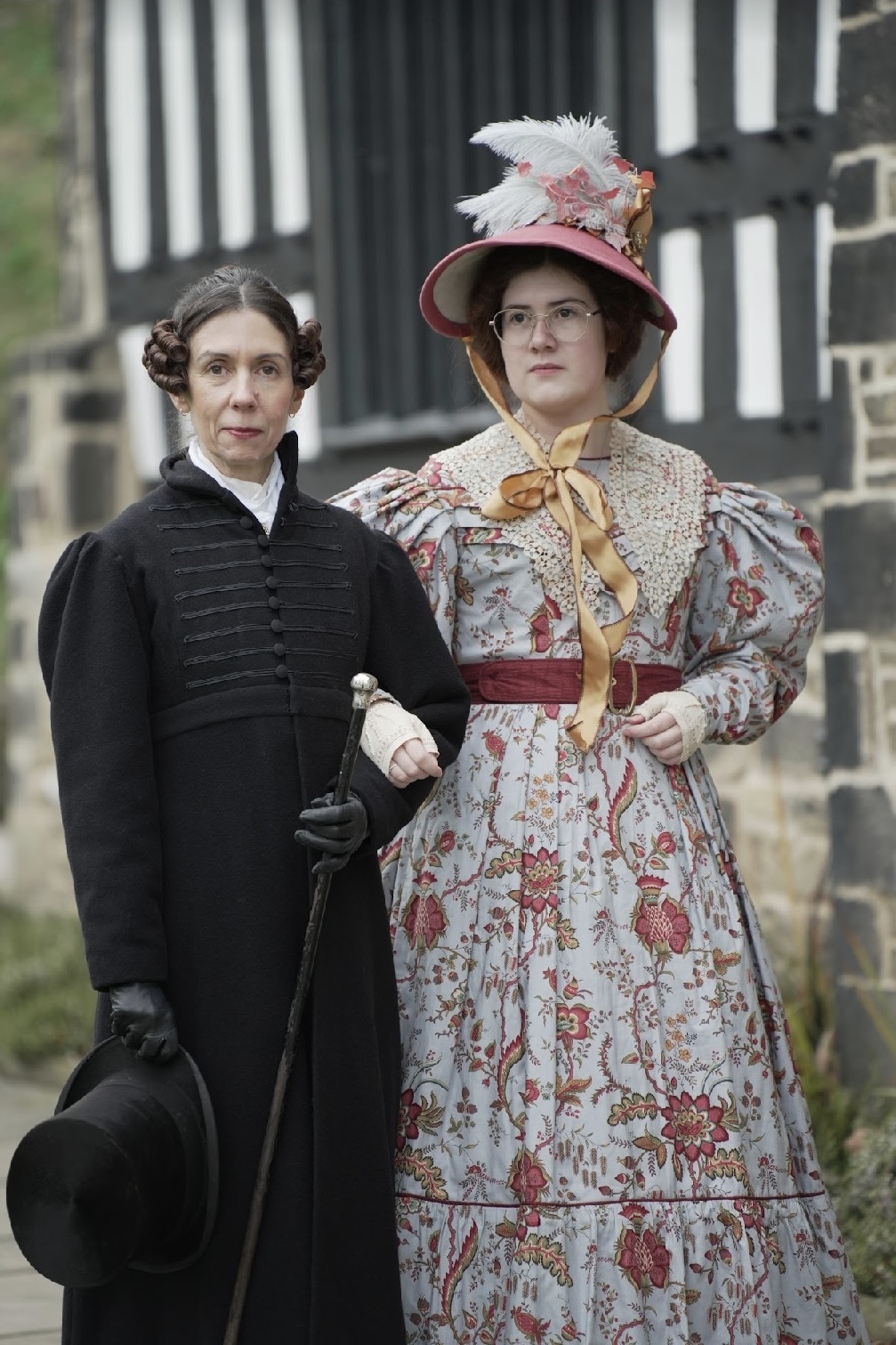 Two people in Regency era costume, one dressed as Anne Lister, standing arm in arm and posing for a photo.