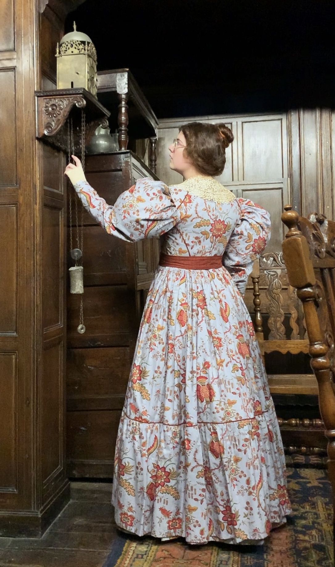 Singer and BA (Hons) Costume student V Joy dressed in 19th century costume. They are standing with their back to the camera and their left arm raised, pointing up at something.