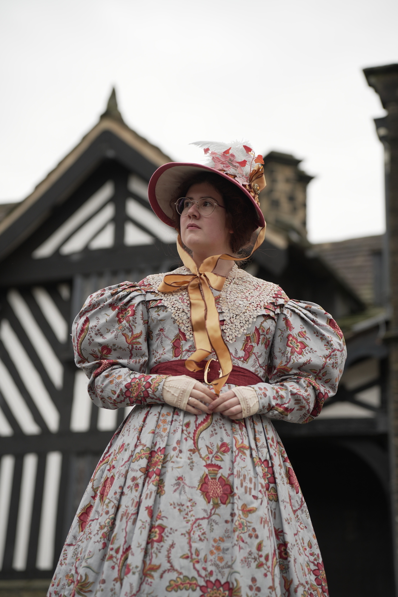 Singer and BA (Hons) Costume student V Joy dressed in 19th century costume, standing outside a Tudor period building, looking off to the left.