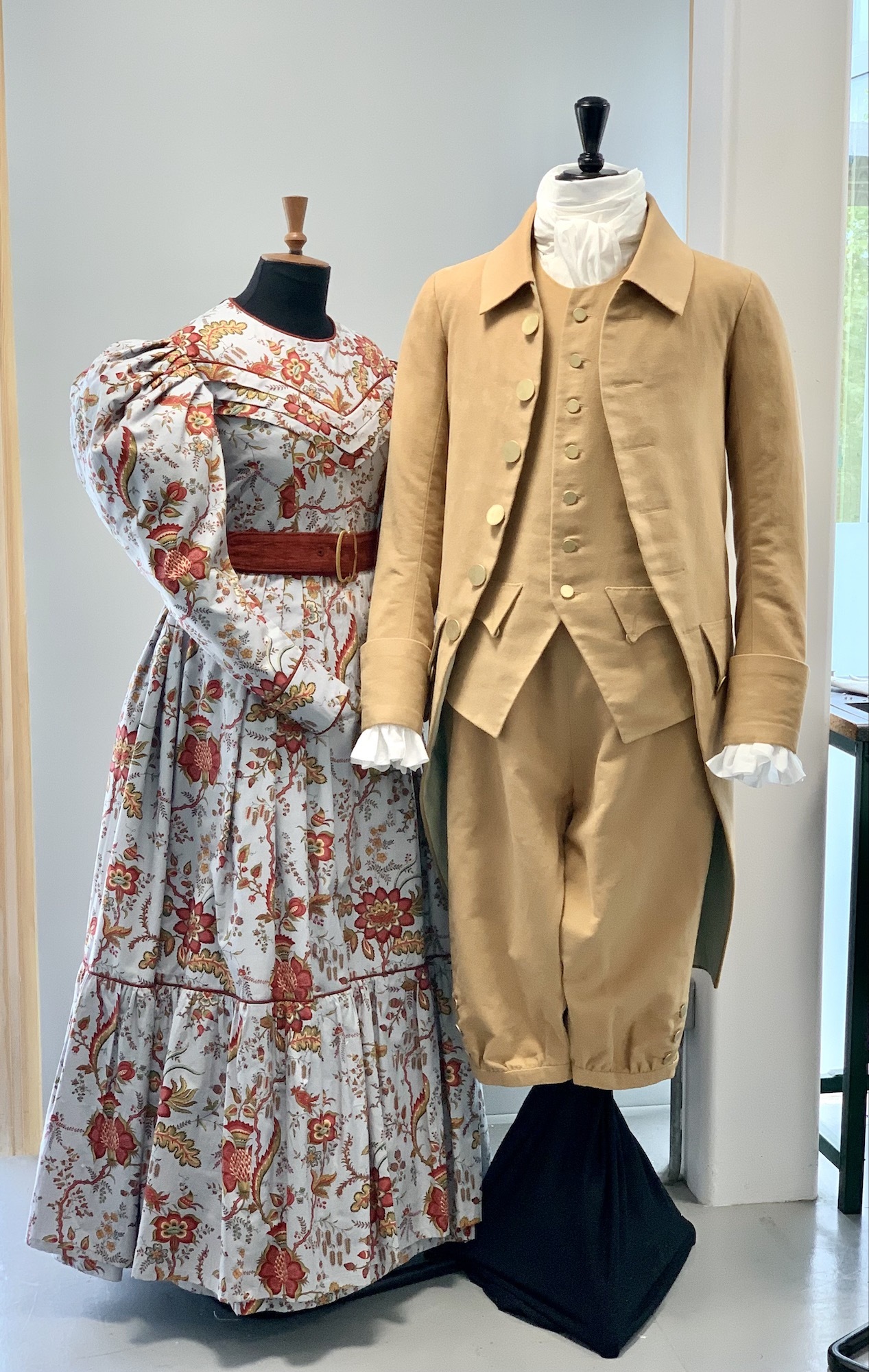 Two period costumes – a dress and a three-piece suit – on display on two mannequins.