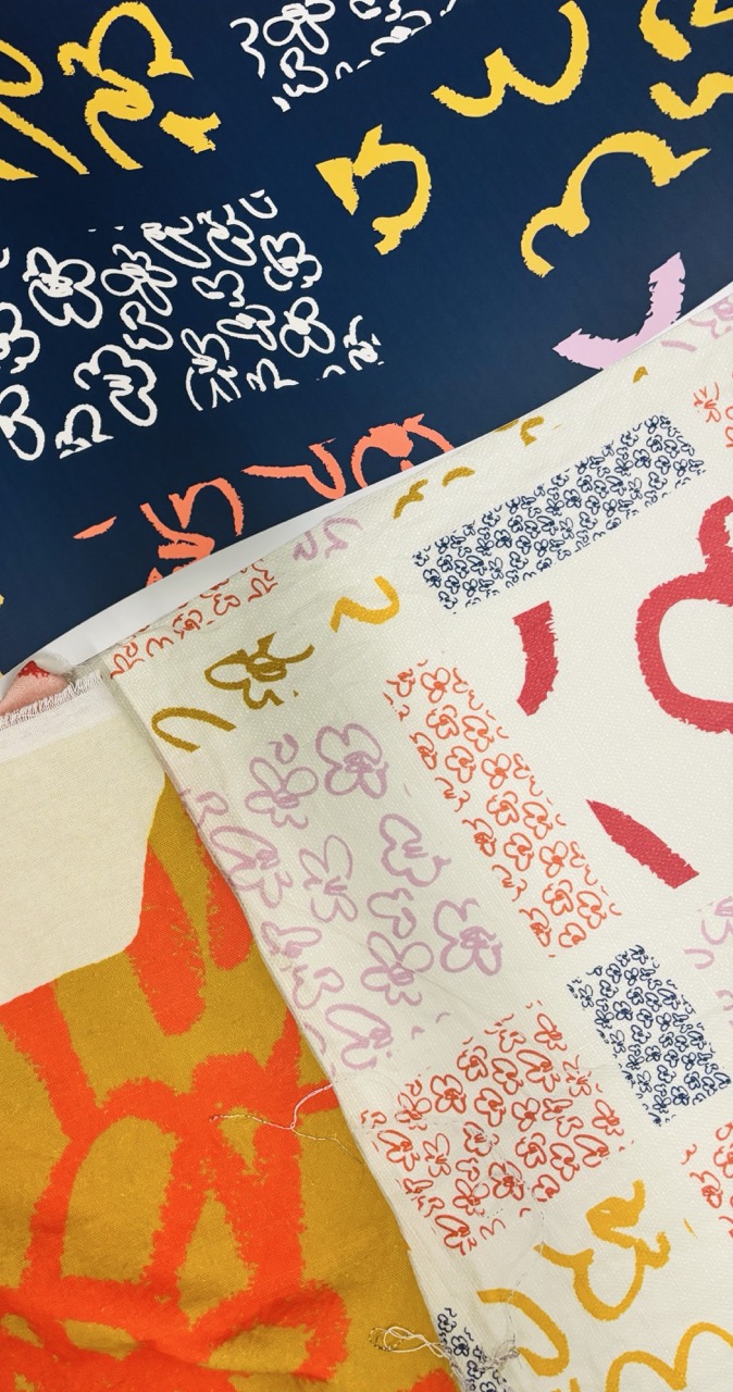 A collection of patterned fabrics arranged in layers. The top layer features a navy background with white abstract shapes, while the lower layers include a yellow-orange fabric, a white one with red and pink designs, and a patterned fabric with small blue squares.