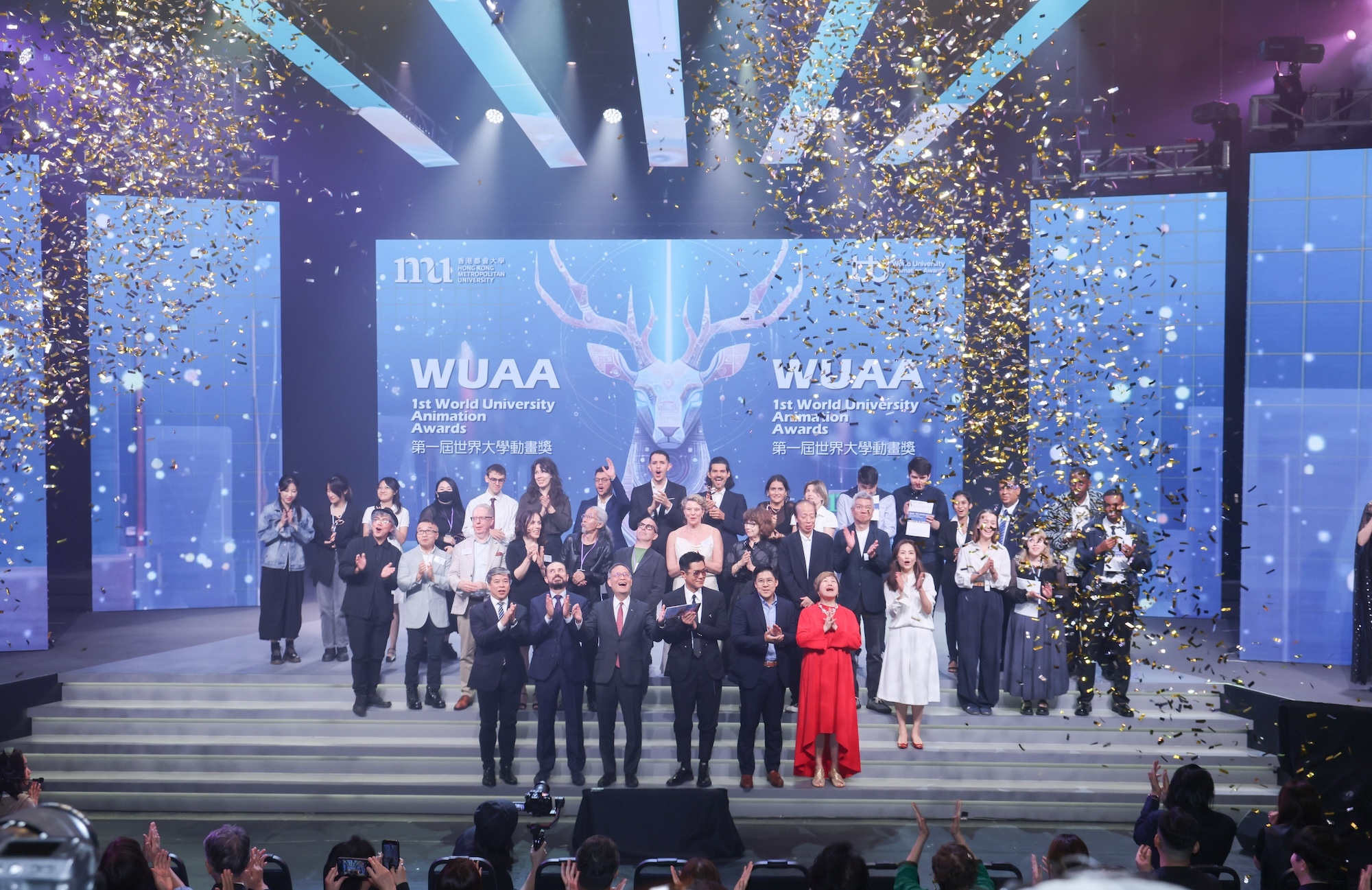 Large group of people in formal attire on stage with blue lighting, confetti falling, and WUAA logos on backdrop screens.