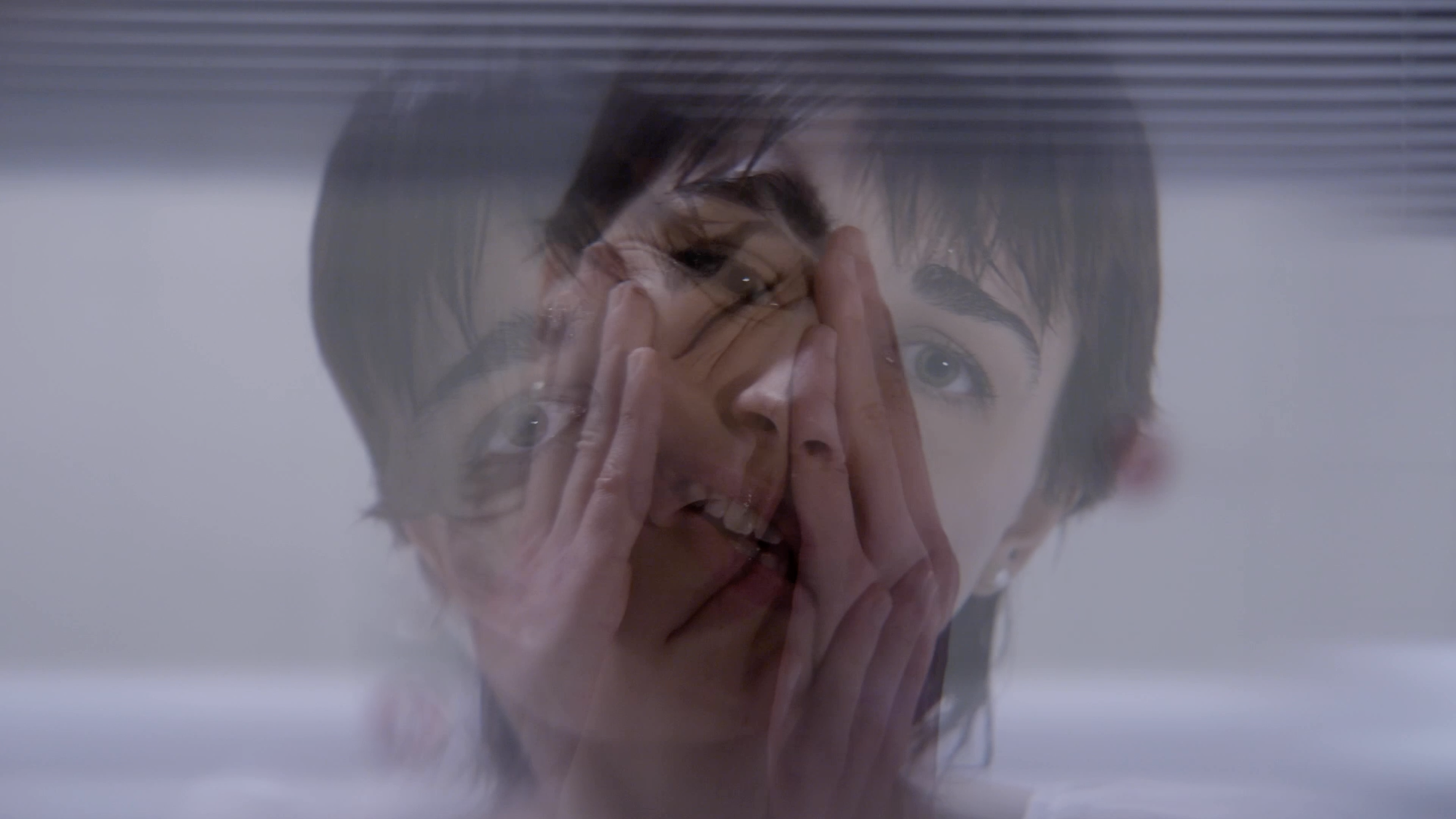 Distorted digital image showing overlapping faces with hands covering them, purple and pink tones with horizontal glitch lines.