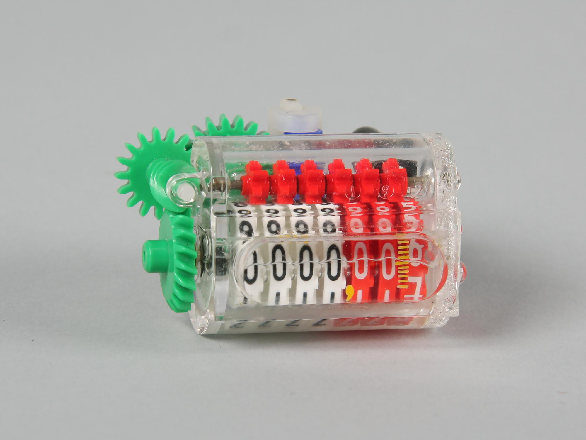 A colourful plastic water meter with a see-through body, showing seven plastic dials with numbers on them.