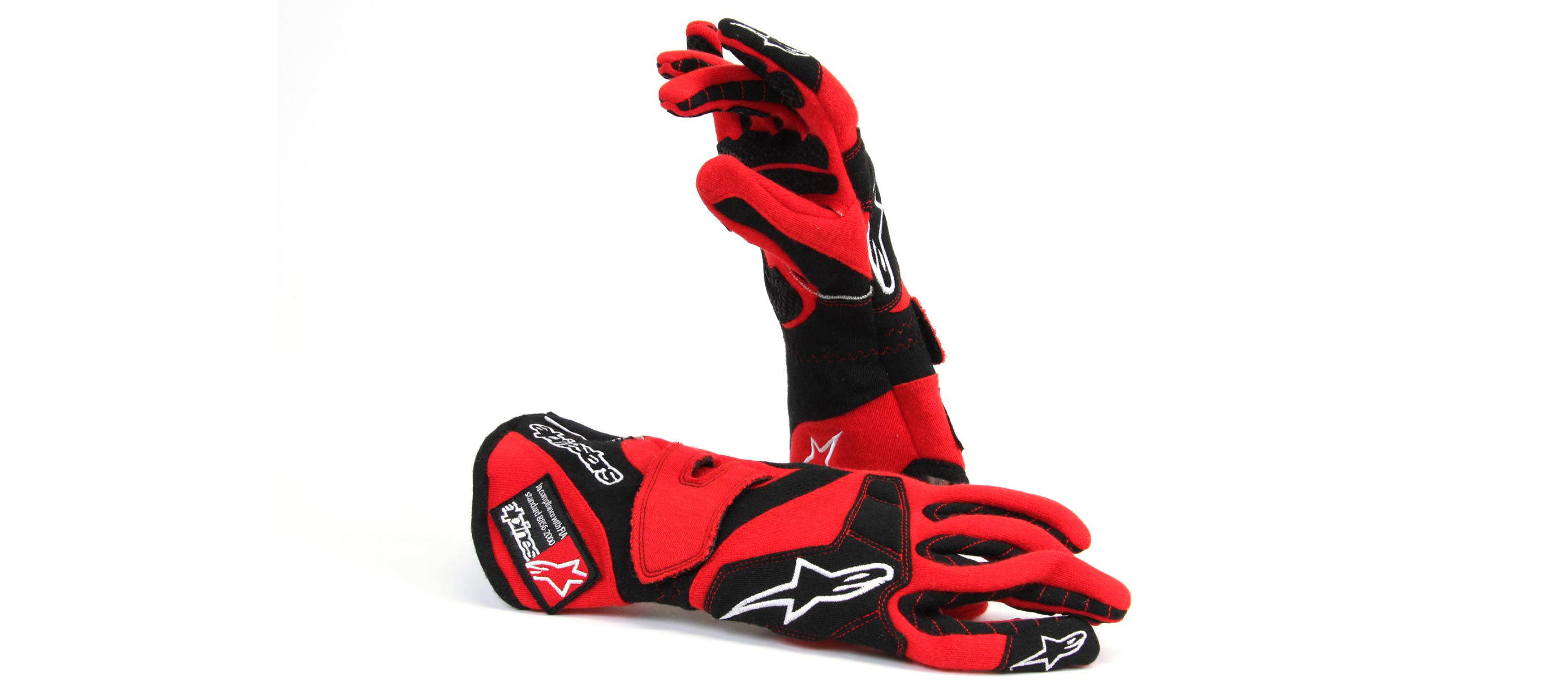 Red and black racing gloves, one lying on a plain surface, the other stood up behind it.