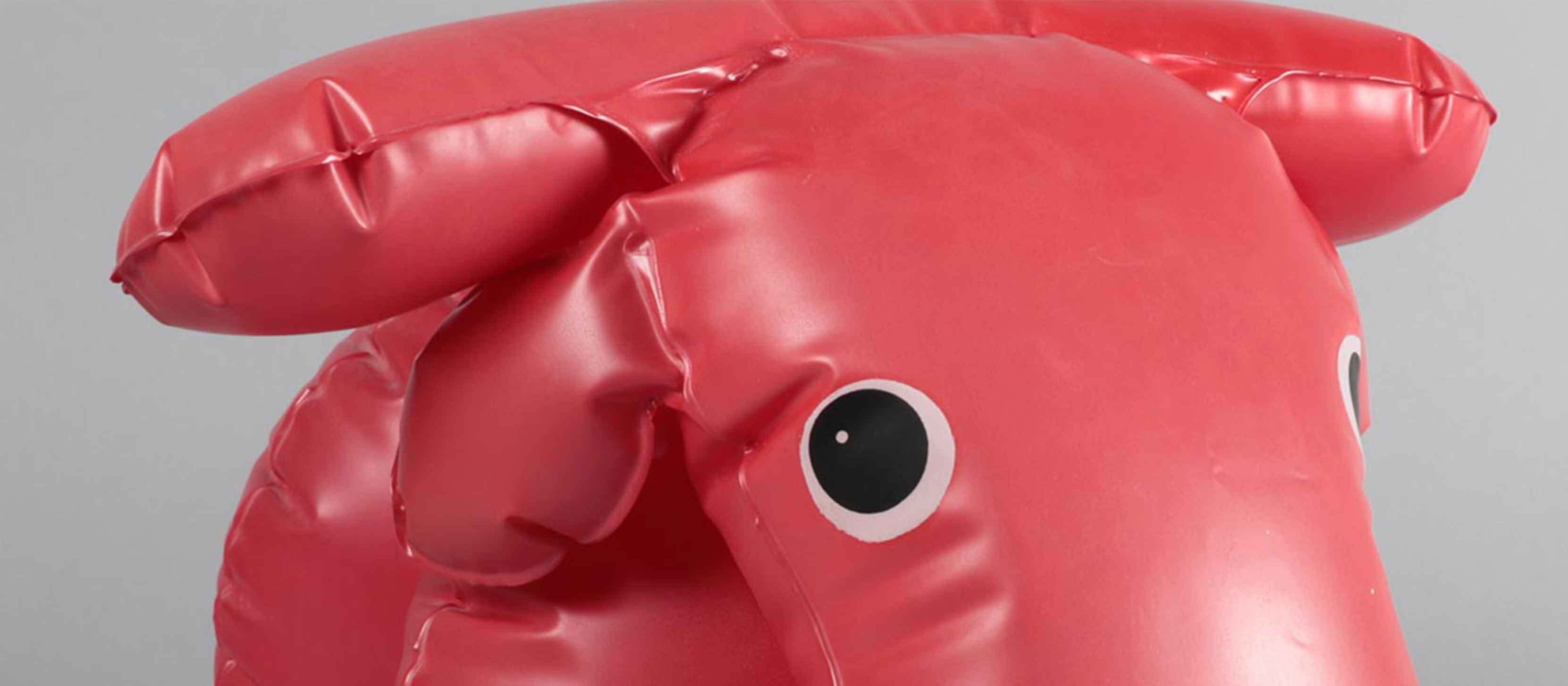 Close-up of an inflatable pink plastic cow toy standing on a plain surface.