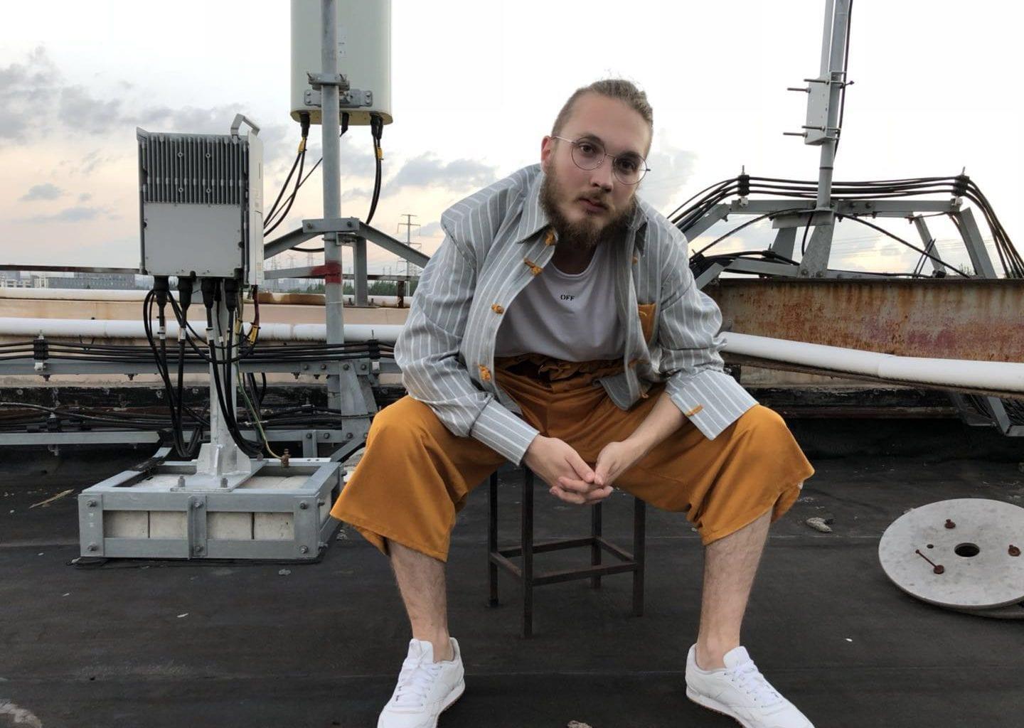 Fashion student sits on a stool on a roof and leans forward