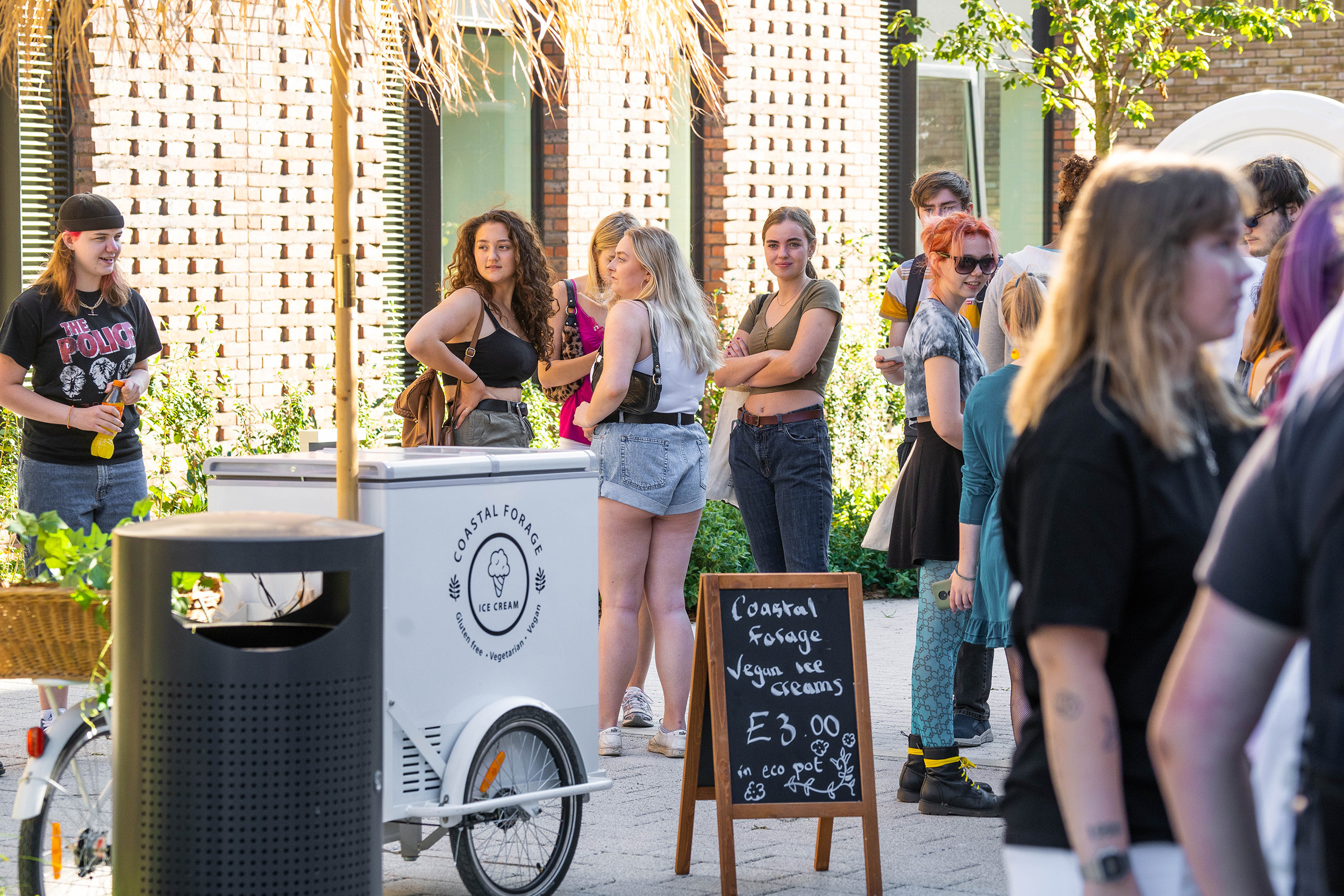 Students mingling outside a university building with an ice cream cart in the foreground.