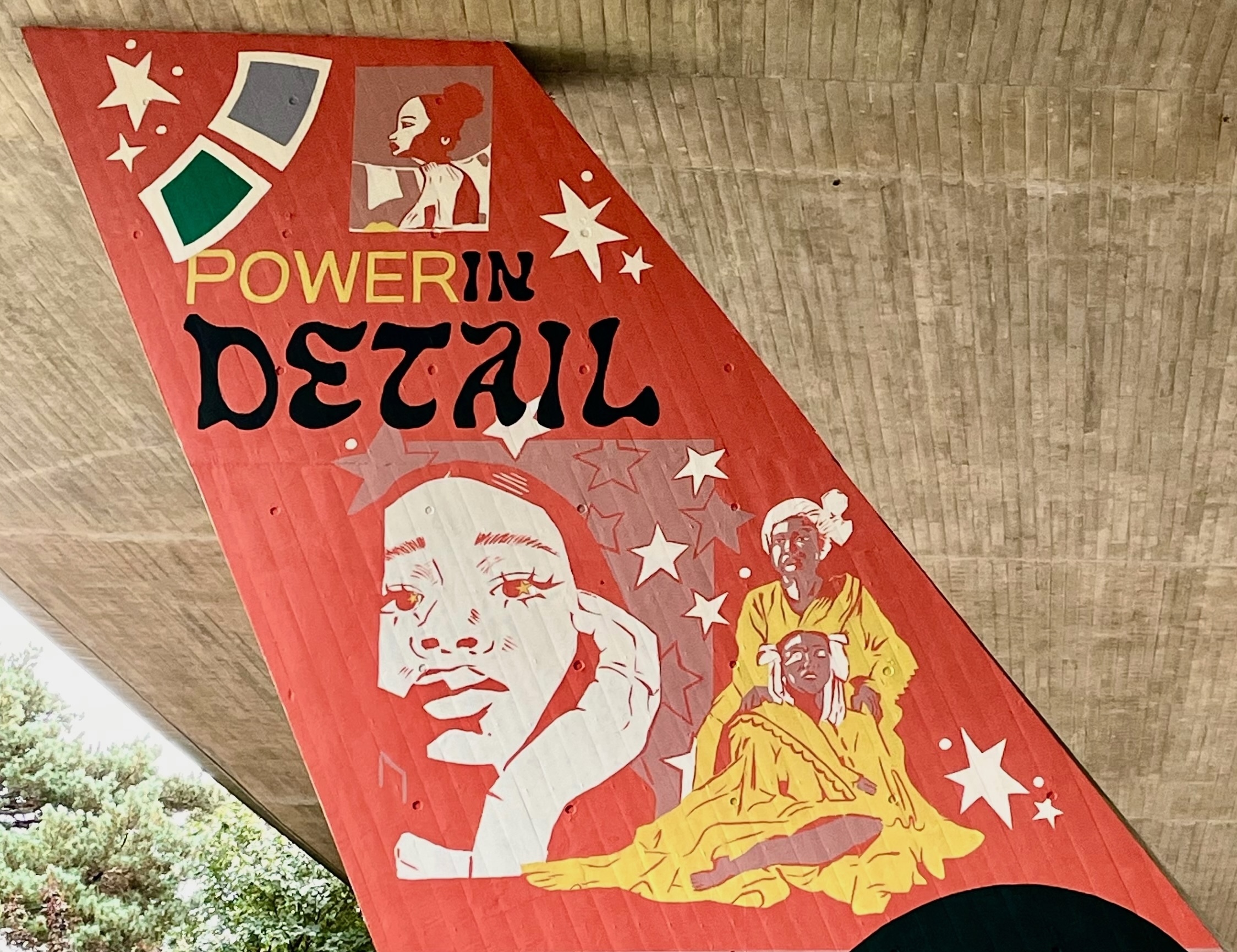 Primarily red mural with white stars and shapes, and illustrations of three people. Text reading "Power in detail" appears off the centre.