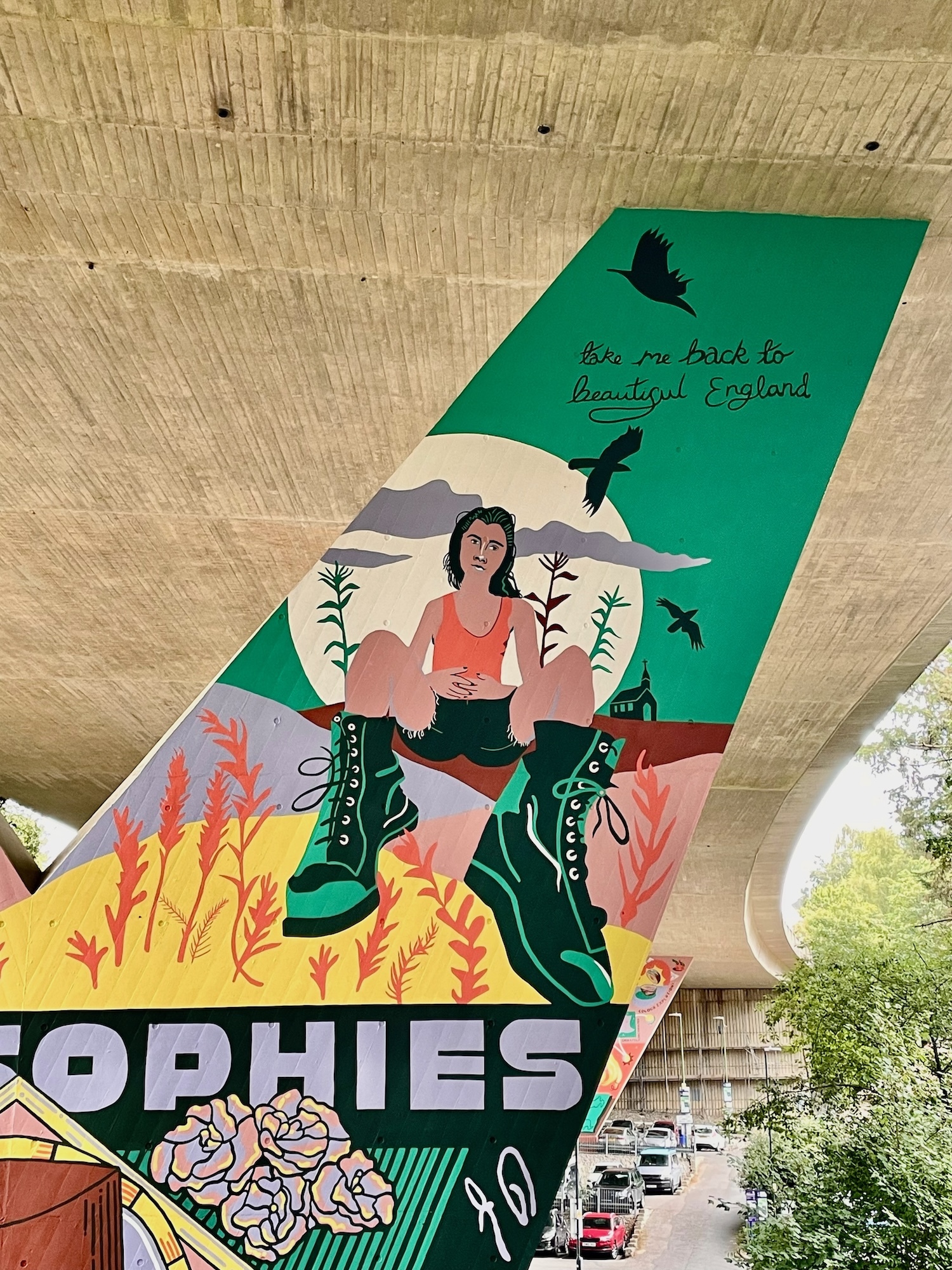 Part of a mural on a flyover pillar wall, depicting a woman sitting, with emphasis on her boots, with a big moon on a green background, and silhouettes of three birds and a church. Text reading "take me back to beautiful England" appears in a handwritten style near the top.